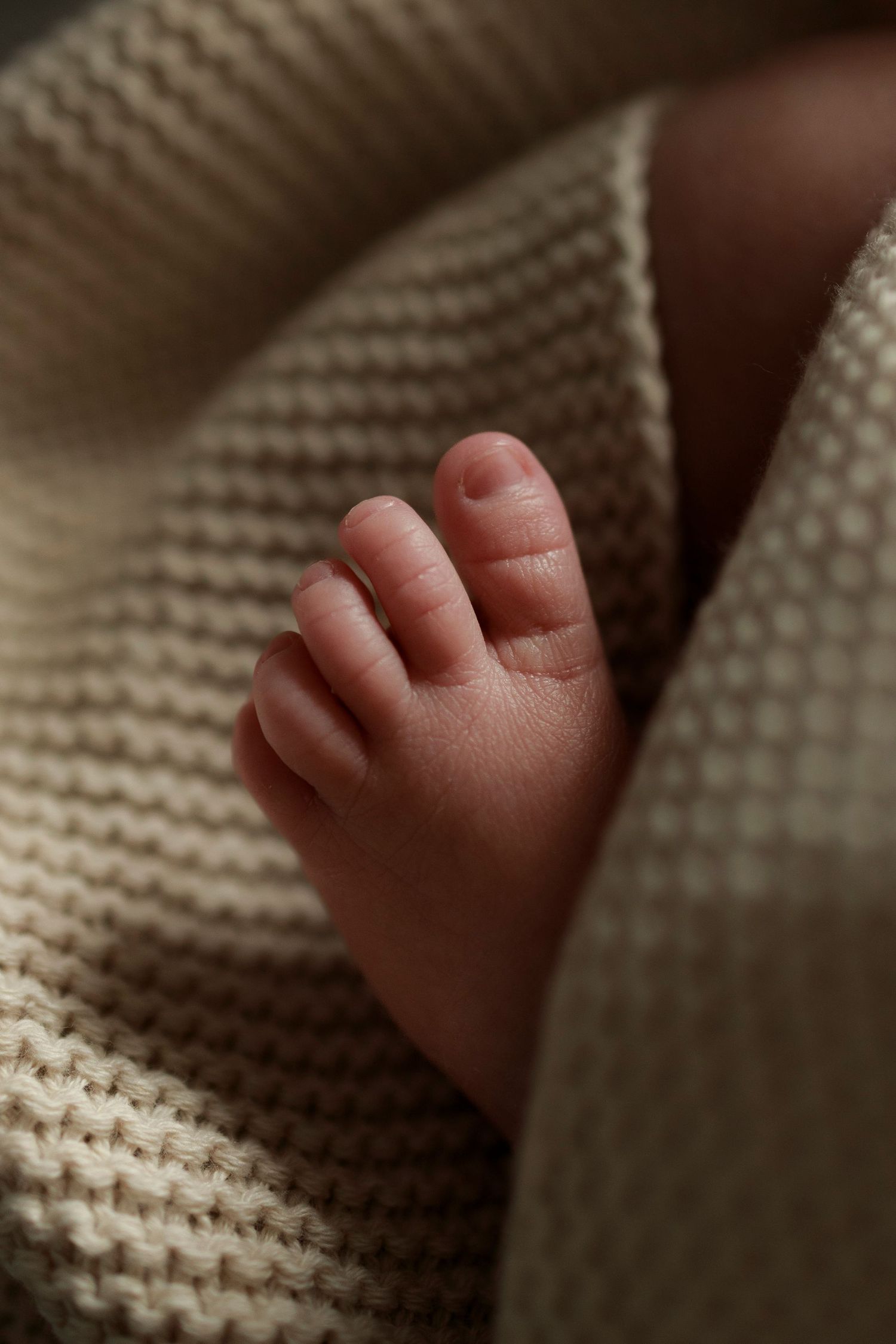 a newborn baby foot and toes poking out of a beige knitted blanket pointing towards the light
