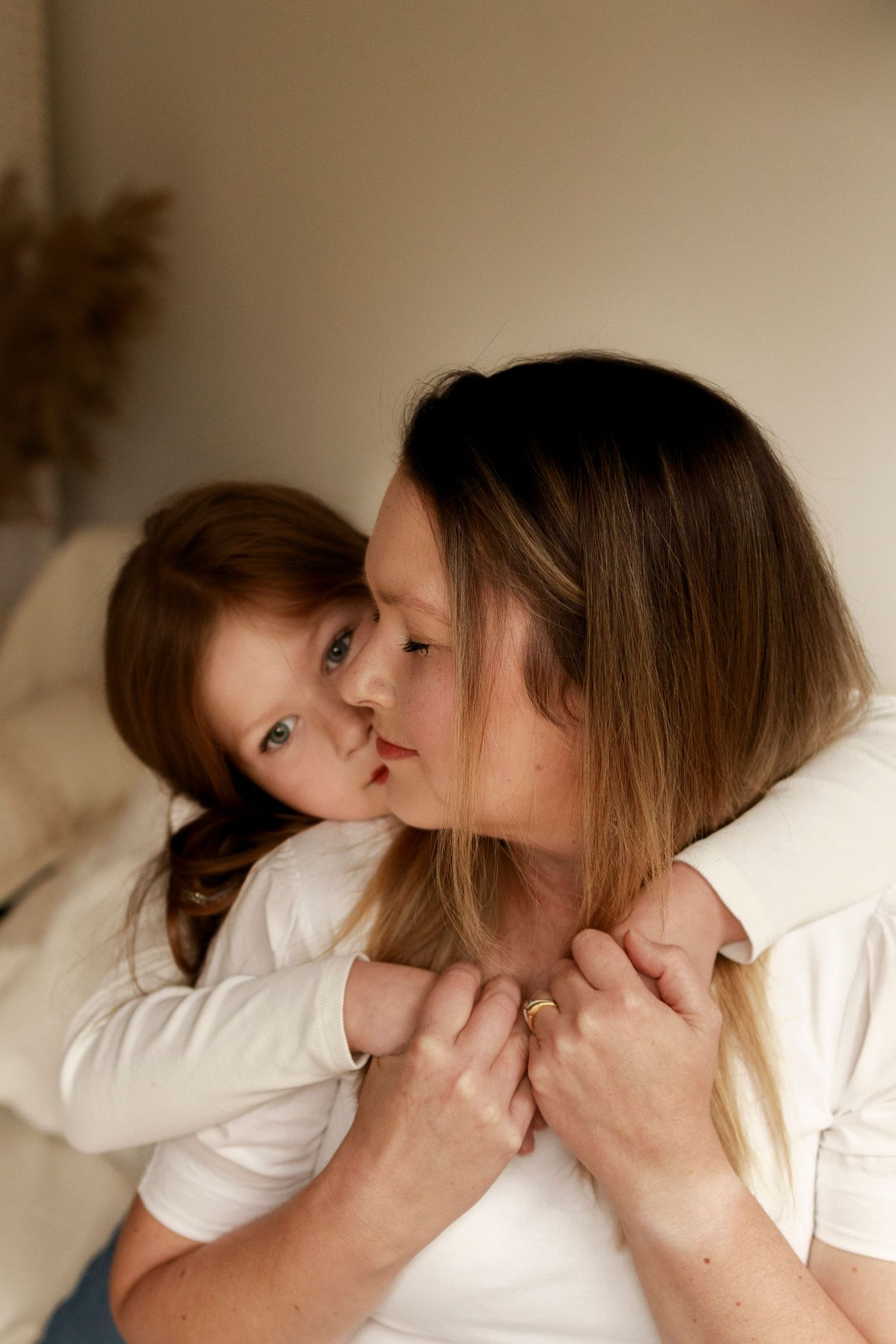 a woman sitting on couch looking over her shoulder with eyes closed holding the hands of a young girl over her neck