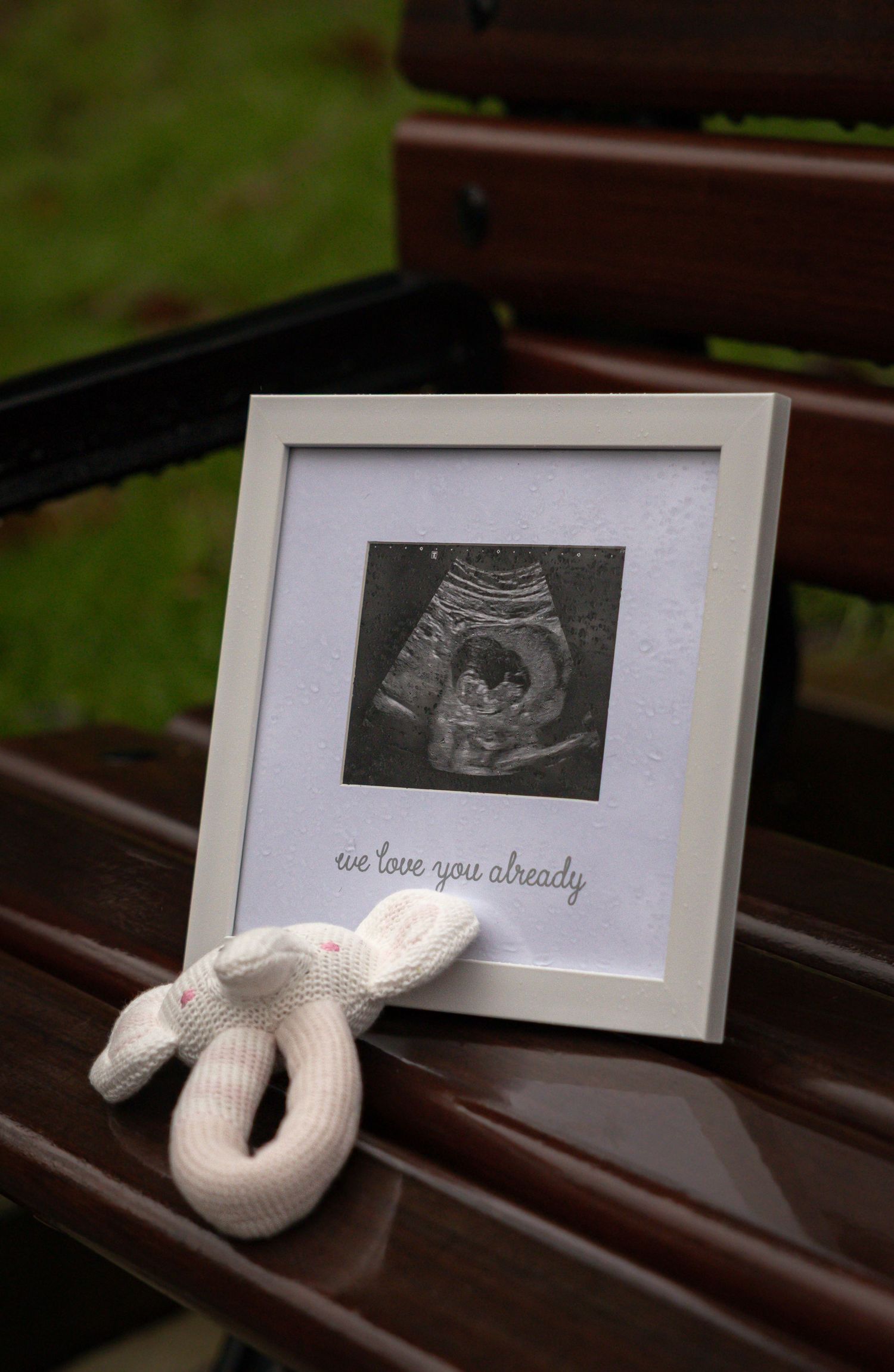 A series of ultrasound photos displayed on wooden benches with a white knitted baby blanket creating a heartwarming pregnancy reveal.