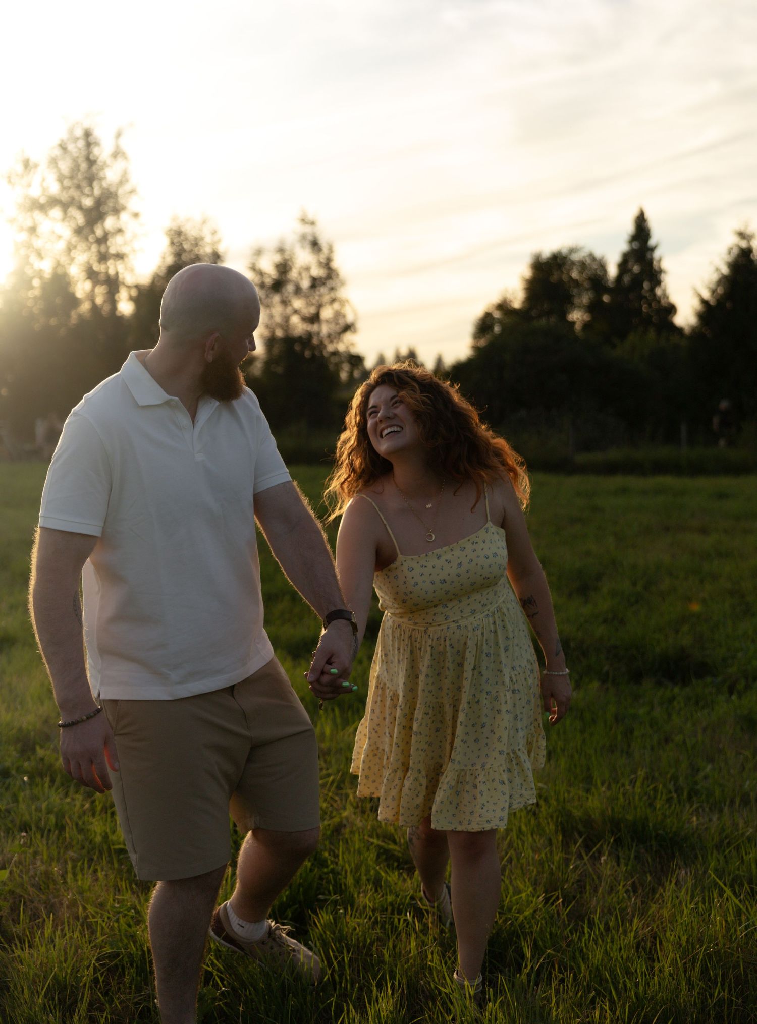 Romantic engagement session at golden hour featuring a couple walking through a grassy field in British Columbia.