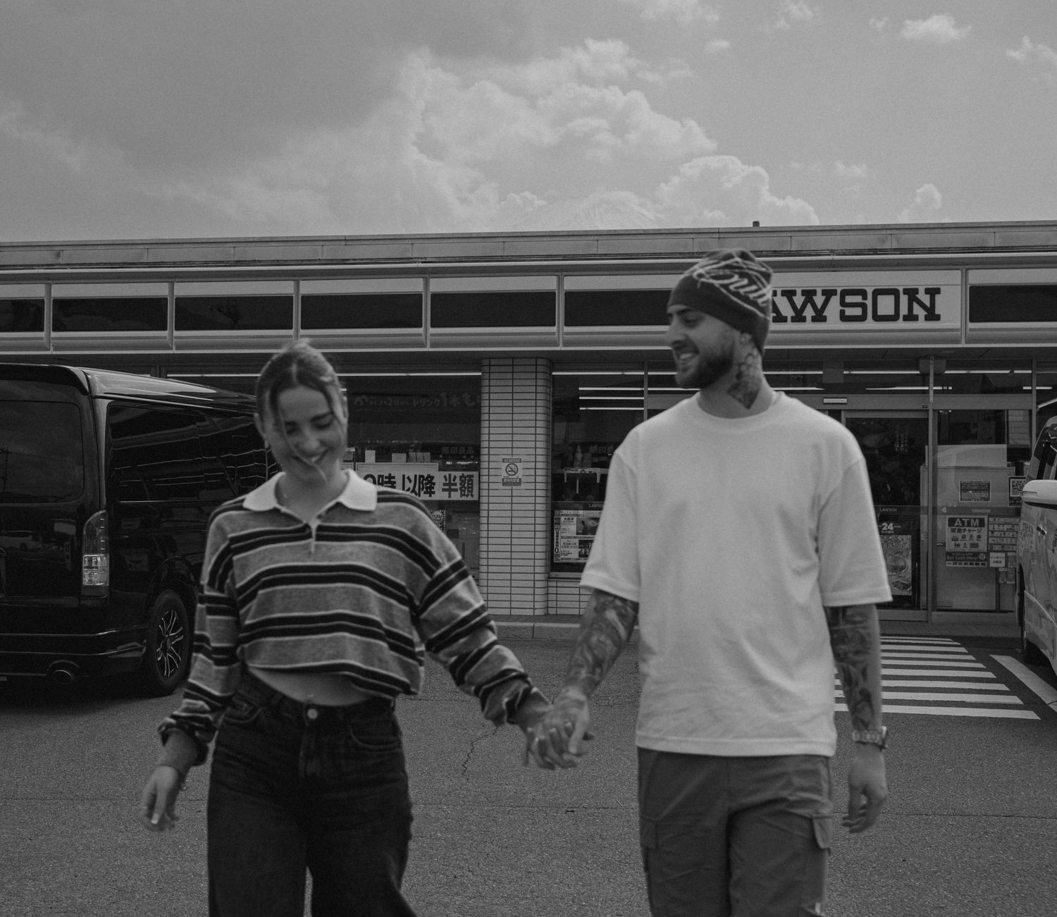 Couple holding hands and smiling outside a Lawson convenience store in Japan, black and white photo.