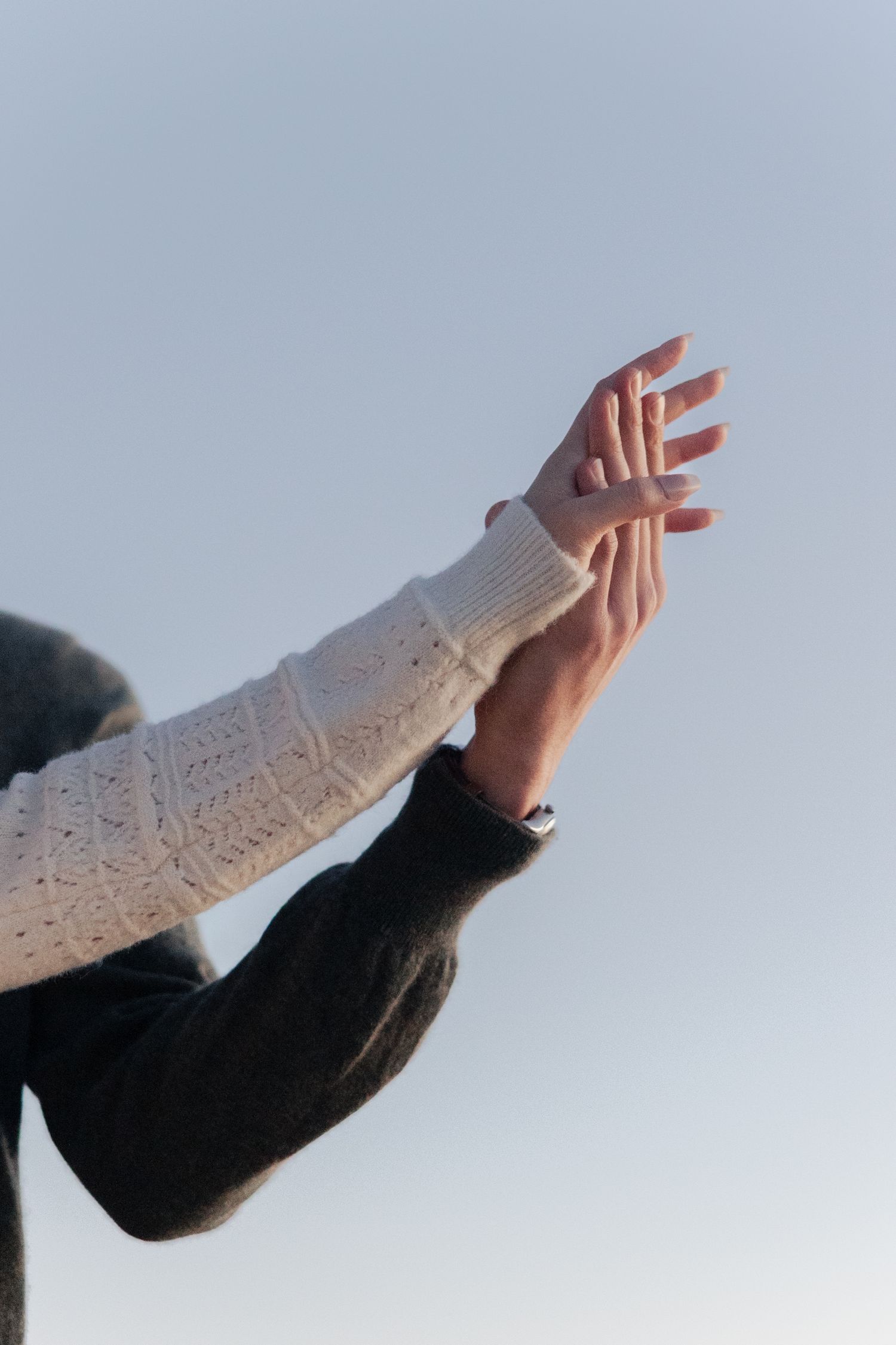 an engaged couple holding hands against a light blue sky background in different graceful positions. Detail shot for an engagement gallery.