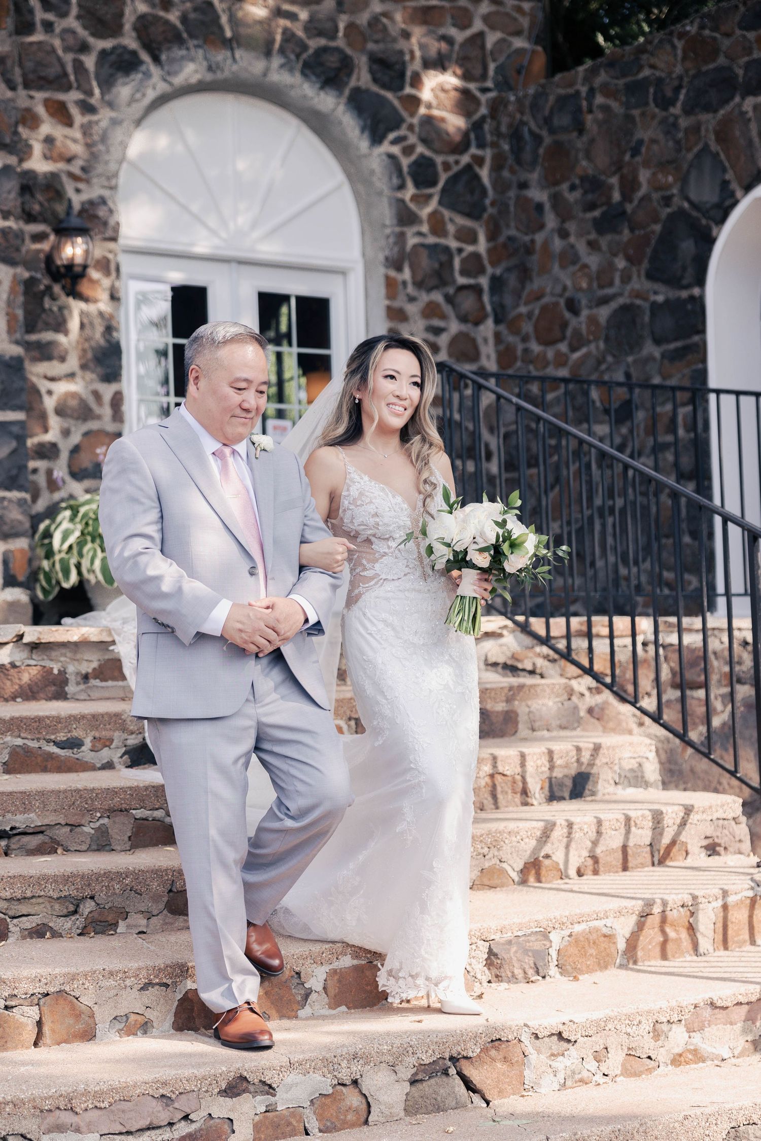 Wedding couple poses on rustic stone steps against a stone wall background.