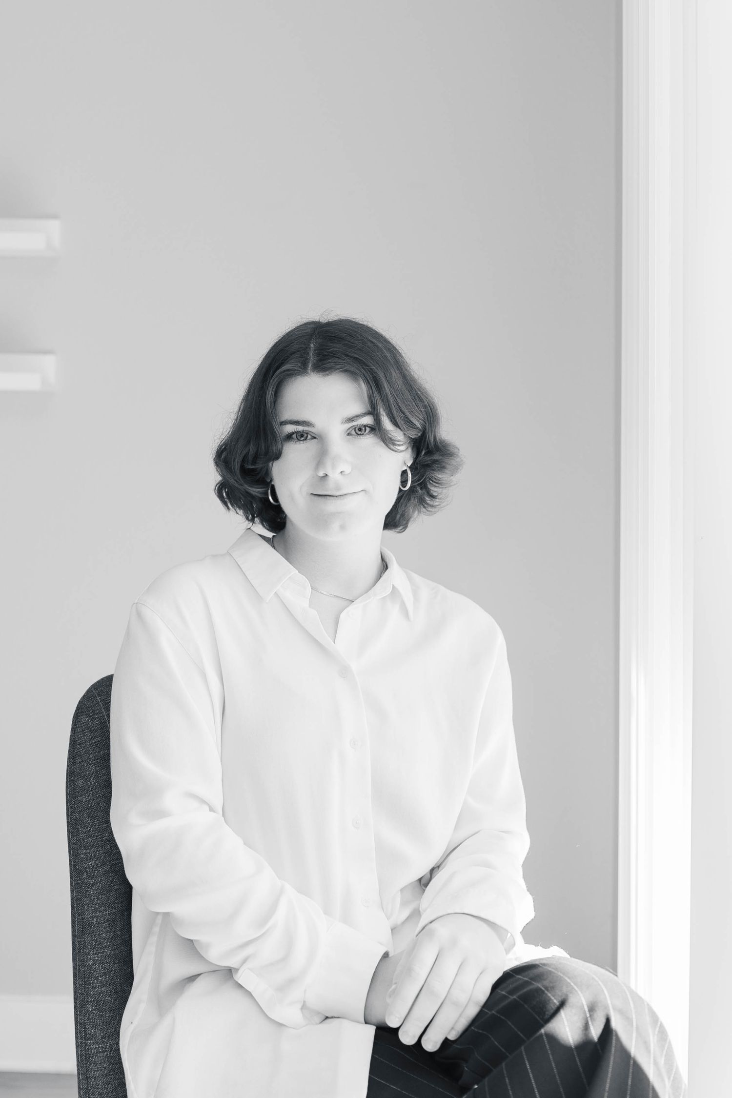 Black and white classic portrait of your wedding photographer in a crisp white button-down shirt seated against a light wall.