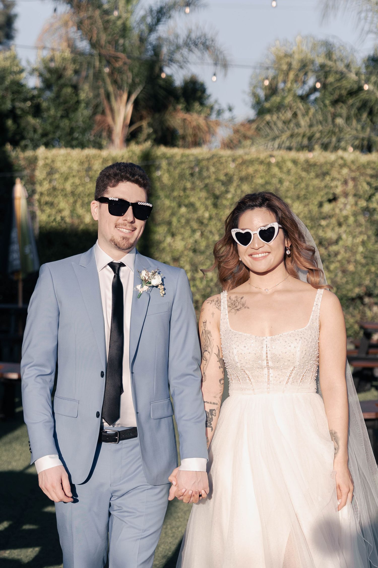 Wedding couple wearing sunglasses pose together in outdoor garden setting.