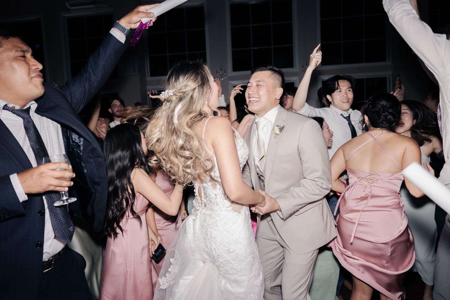 Couple and wedding guests dancing and celebrating with hands raised during reception party.