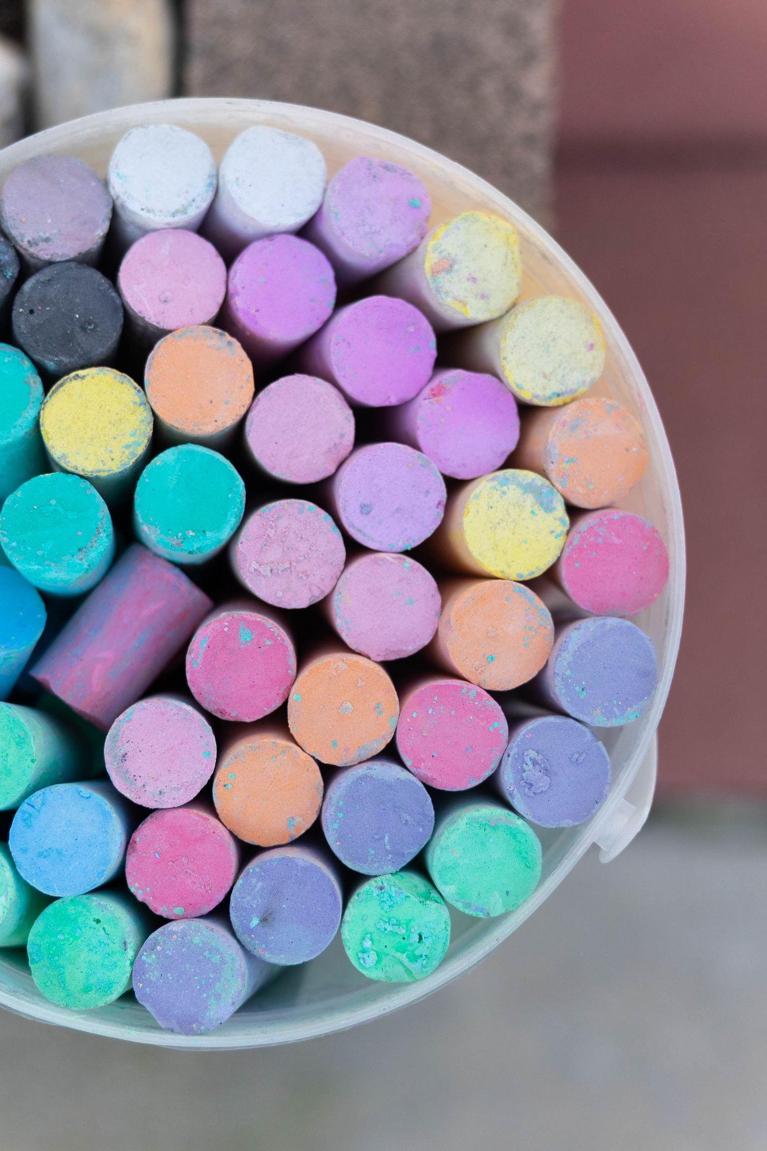 Colorful sidewalk chalk pieces in pastel shades of blue, pink, yellow and purple arranged in rows on a white surface.