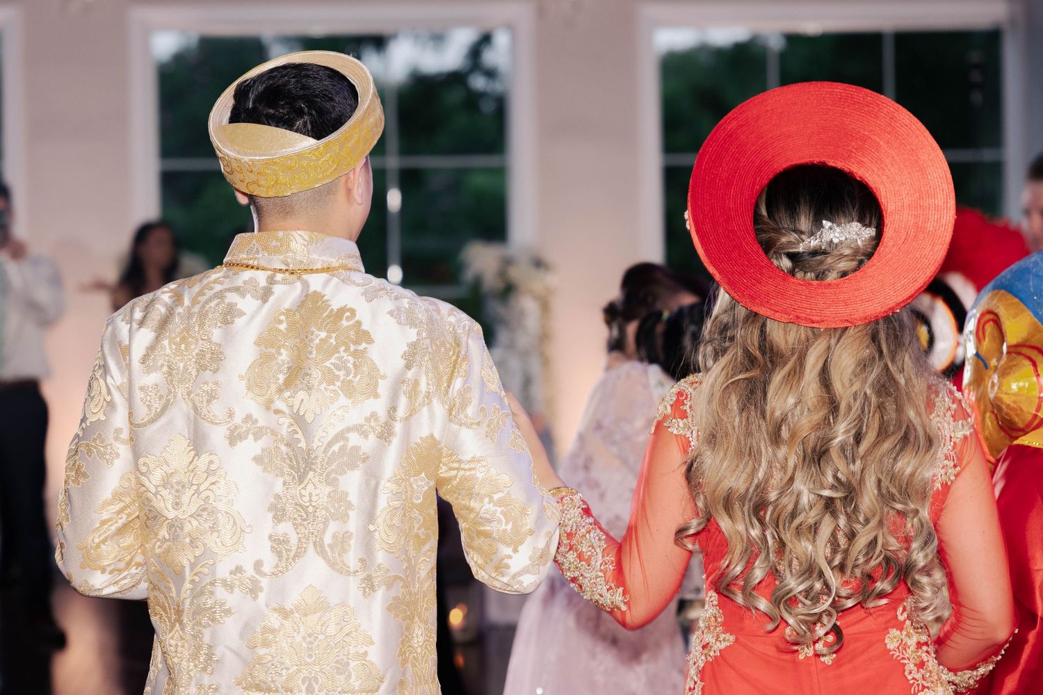 Bride and groom wearing traditional Vietnamese ceremonial outfits seen from behind during their wedding celebration.