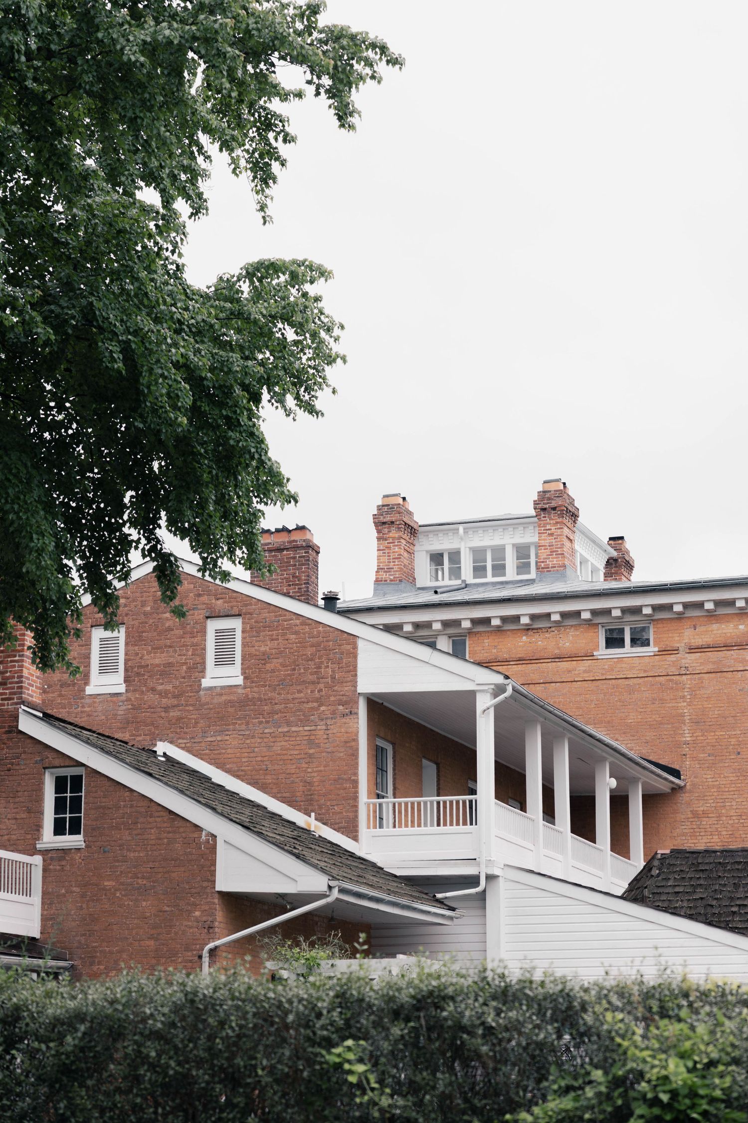 Architectural detail showing white dormers and red brick buildings with chimneys against a cloudy sky.