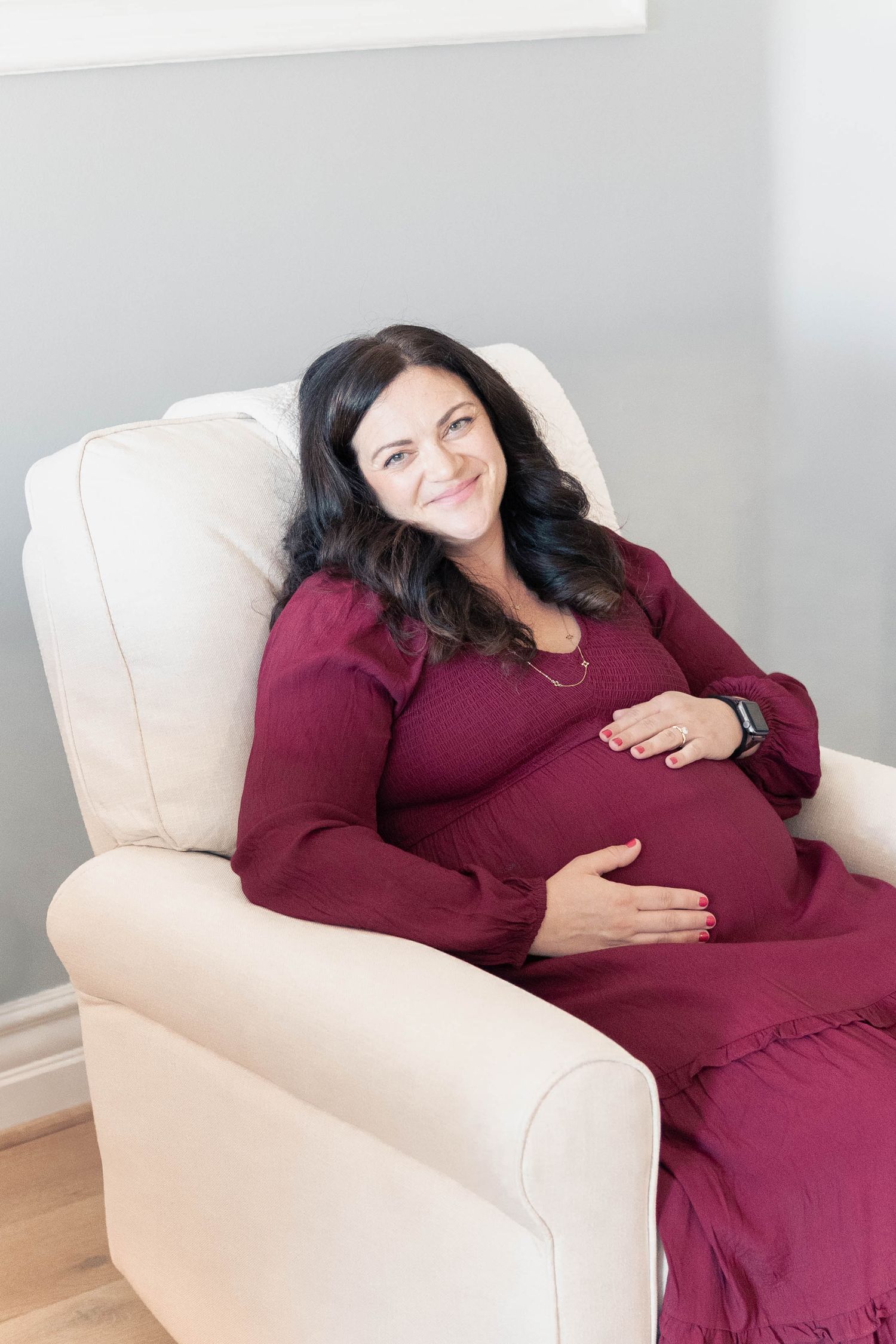 Someone in a burgundy dress relaxes comfortably on a cream-colored armchair.