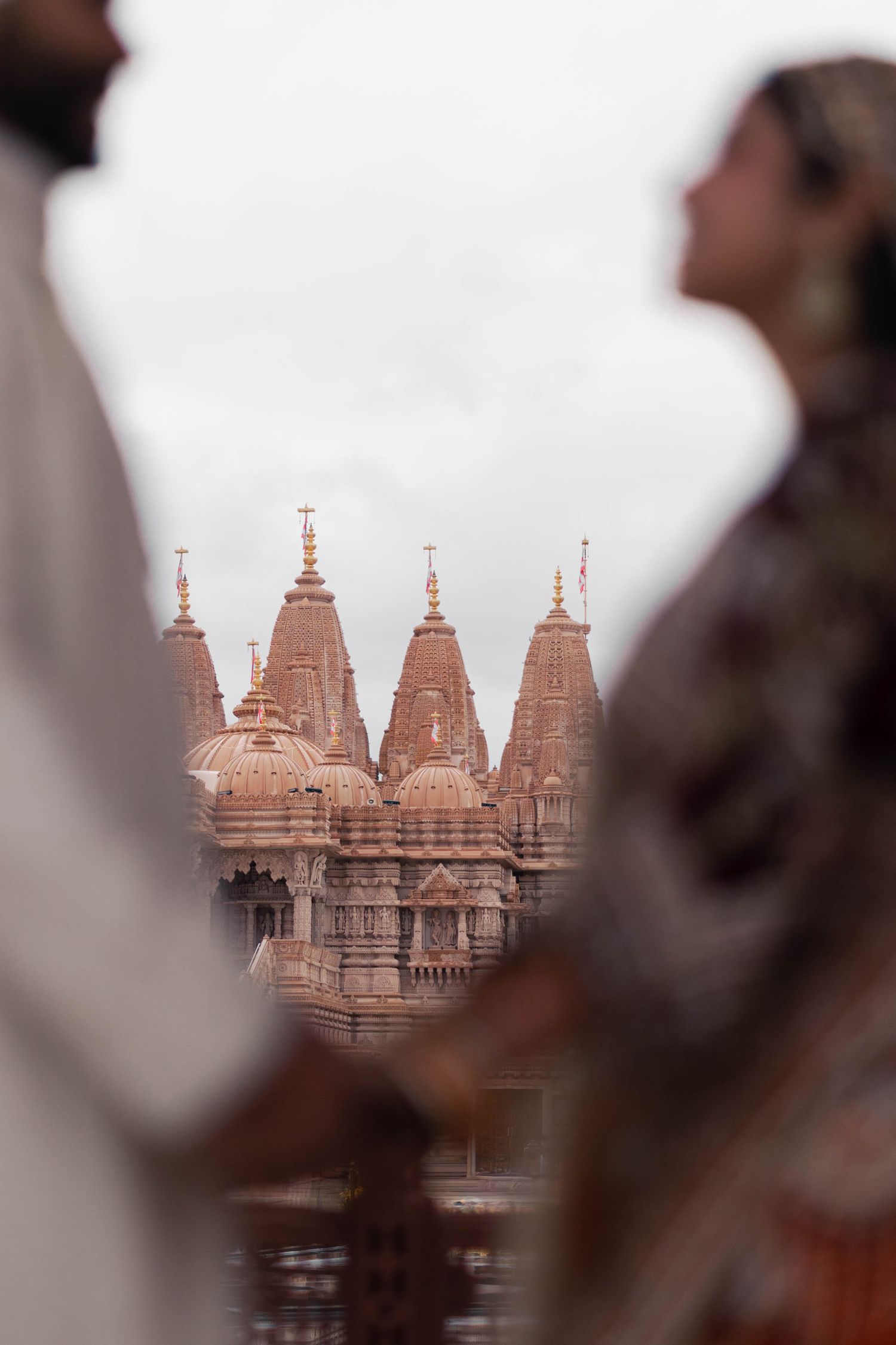 Ancient Hindu temple spires with ornate architecture rise against a hazy sky in soft pink hues.