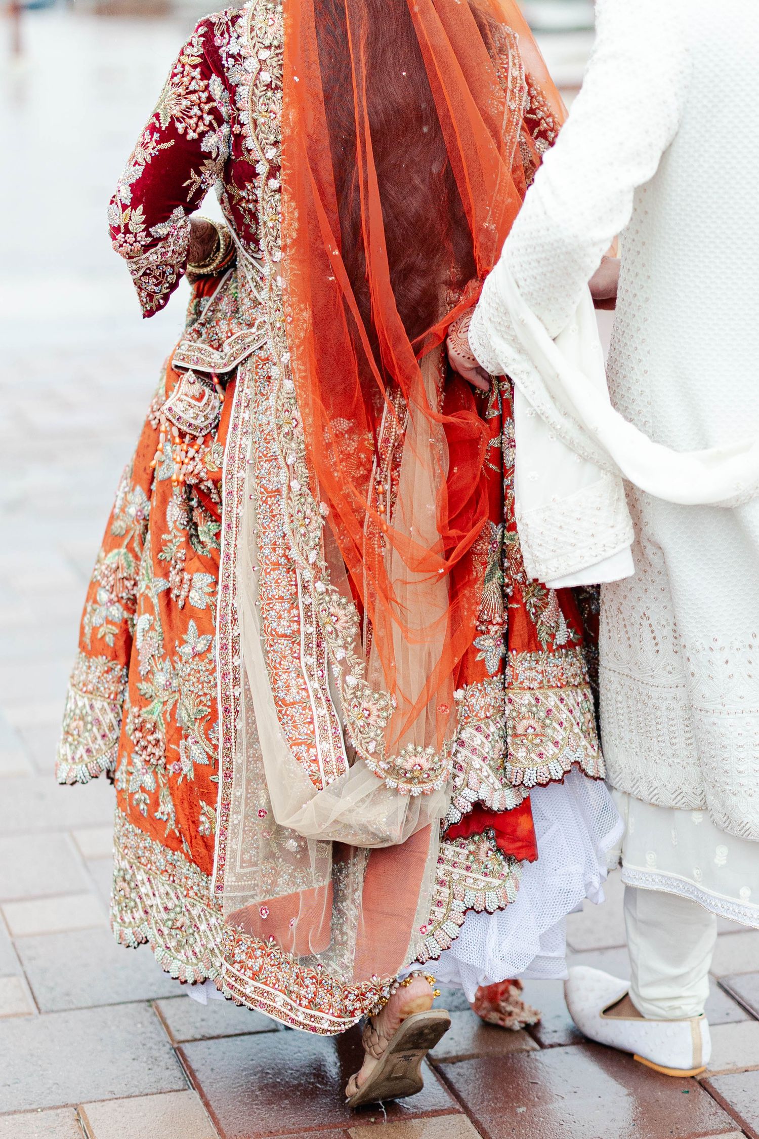 Close-up details of traditional Indian wedding attire showing ornate red and white embroidered lehenga with matching footwear.