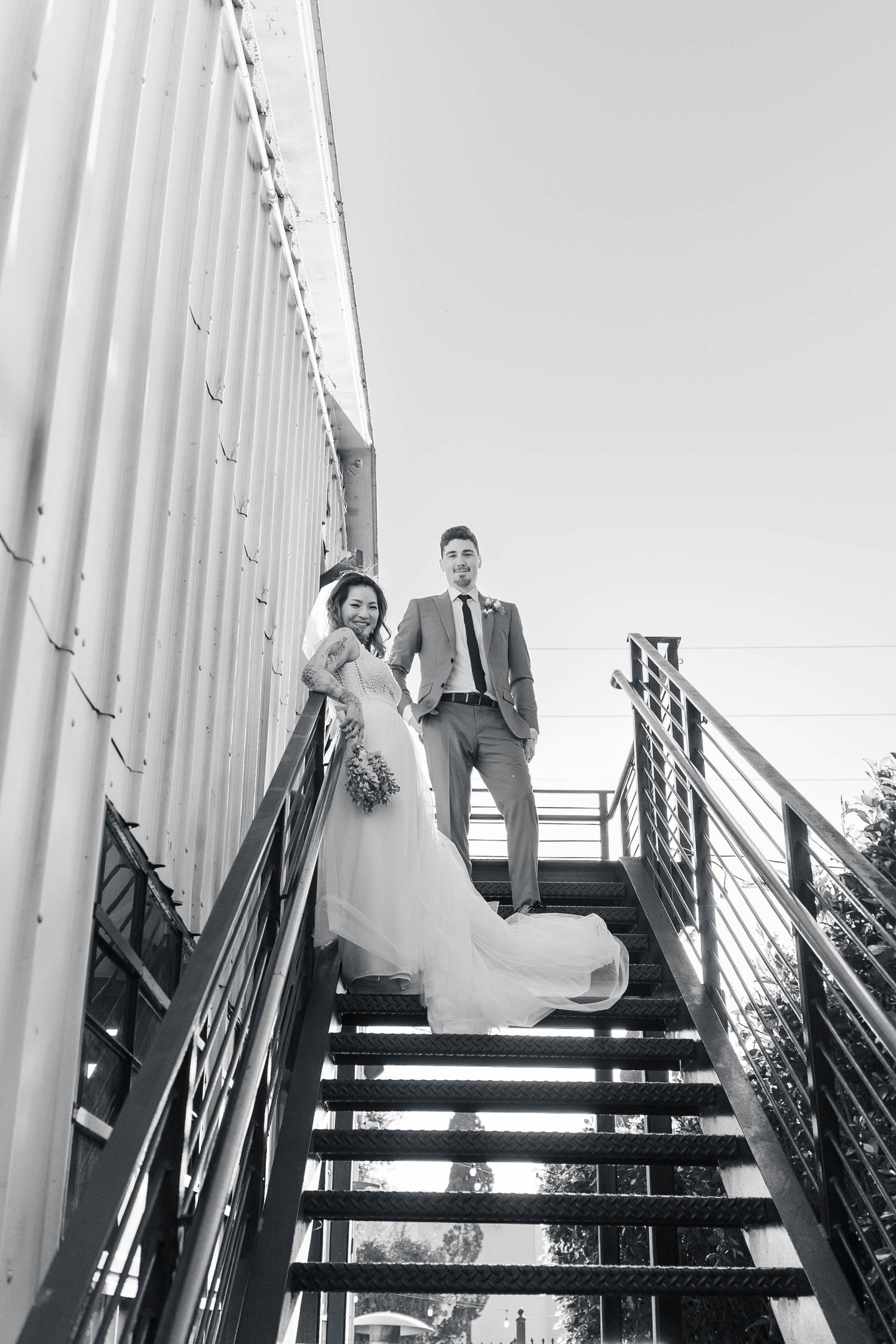 Wedding party poses on modern black stairs between white columns in dramatic black and white composition.