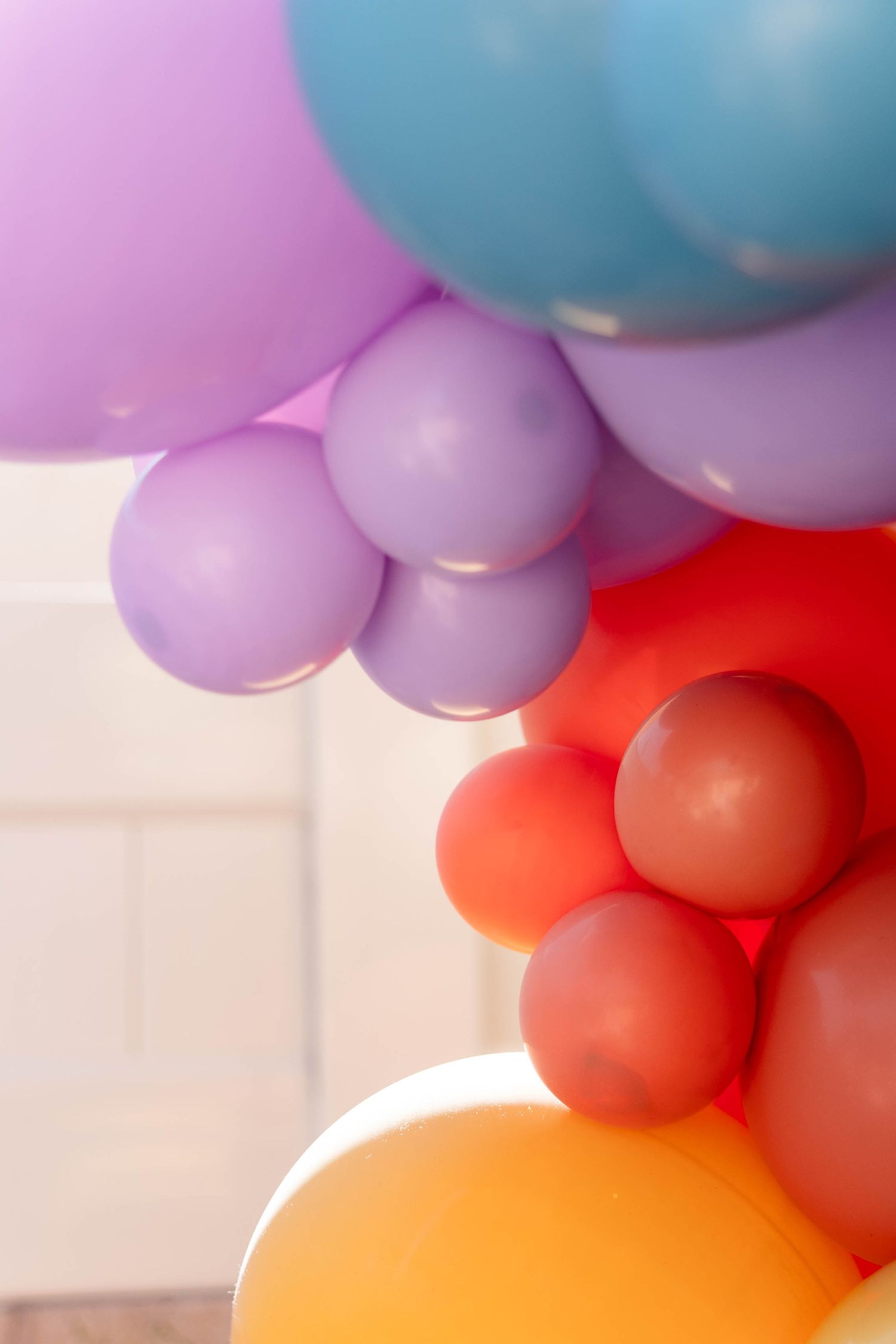 Colorful balloon arch installation featuring pastel pink, blue, orange and red balloons against a white background.
