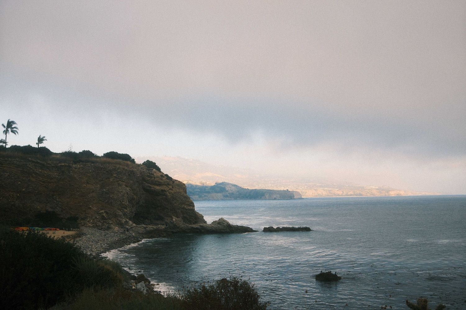 Dramatic coastal cliffs overlook the misty Pacific Ocean during sunset along a rugged shoreline.
