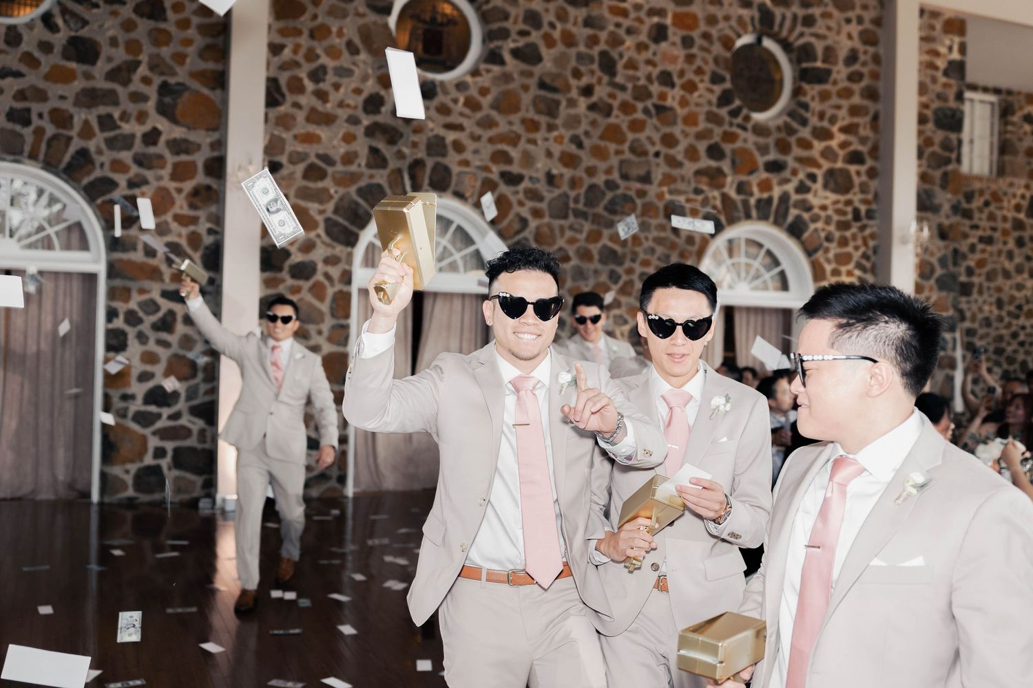 Wedding party wearing sunglasses and posing against stone wall backdrop.