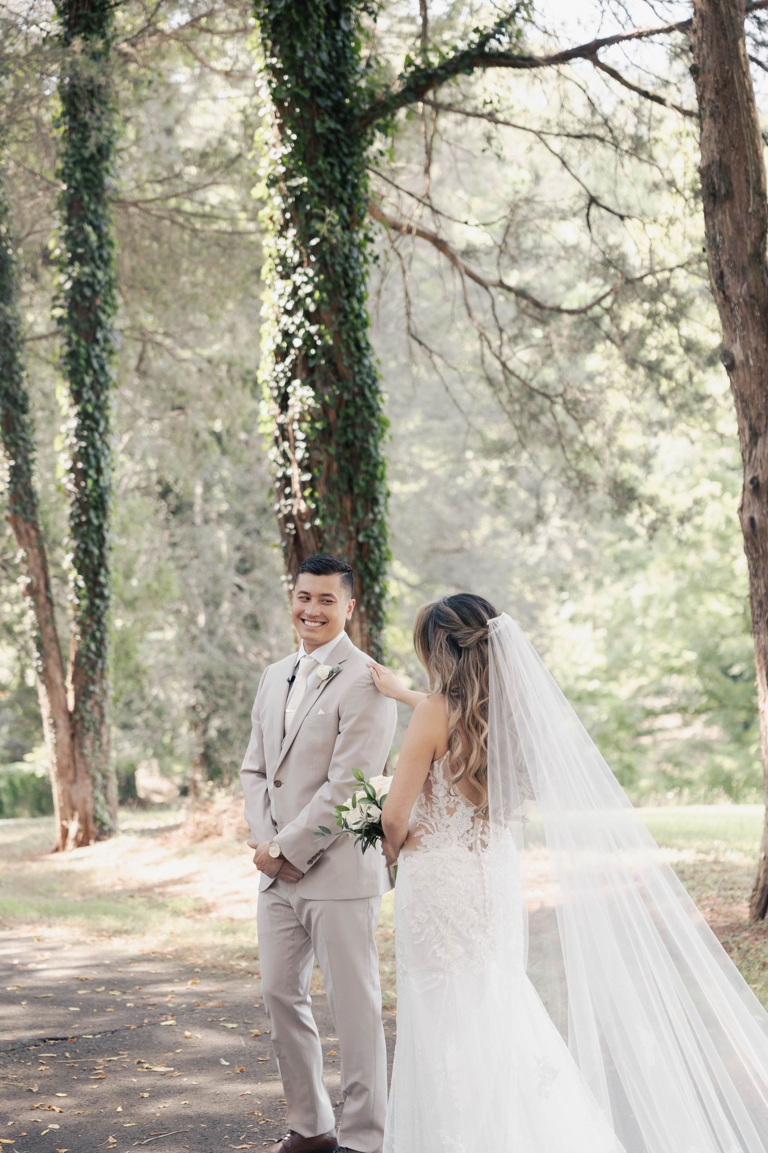 Newlyweds share a joyful moment in a forest setting with ivy-covered trees.
