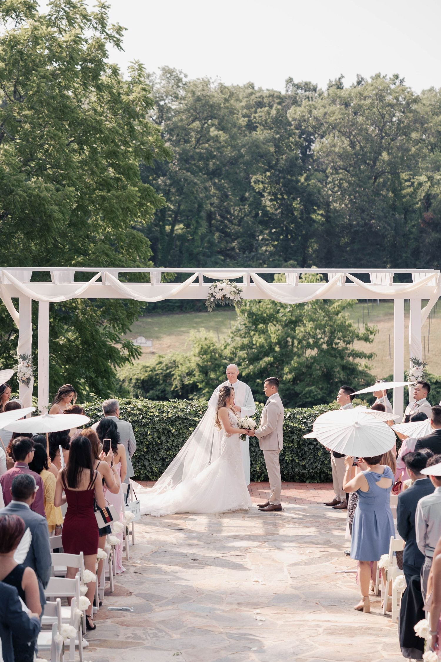 Wedding guests holding white parasols during outdoor ceremony.