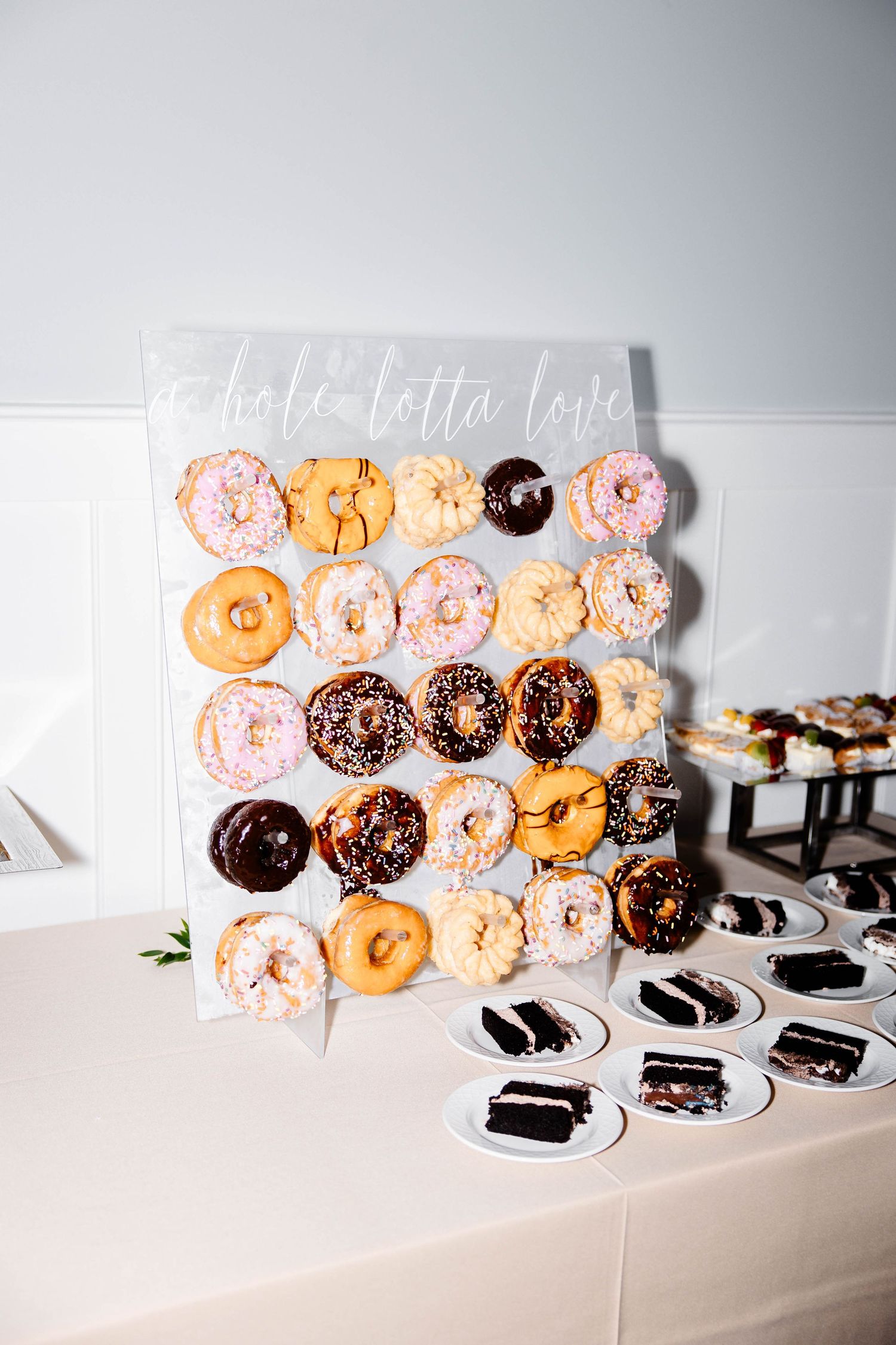 Assorted donuts arranged on a white wall display with chocolate and pink frosted varieties against a minimalist background.
