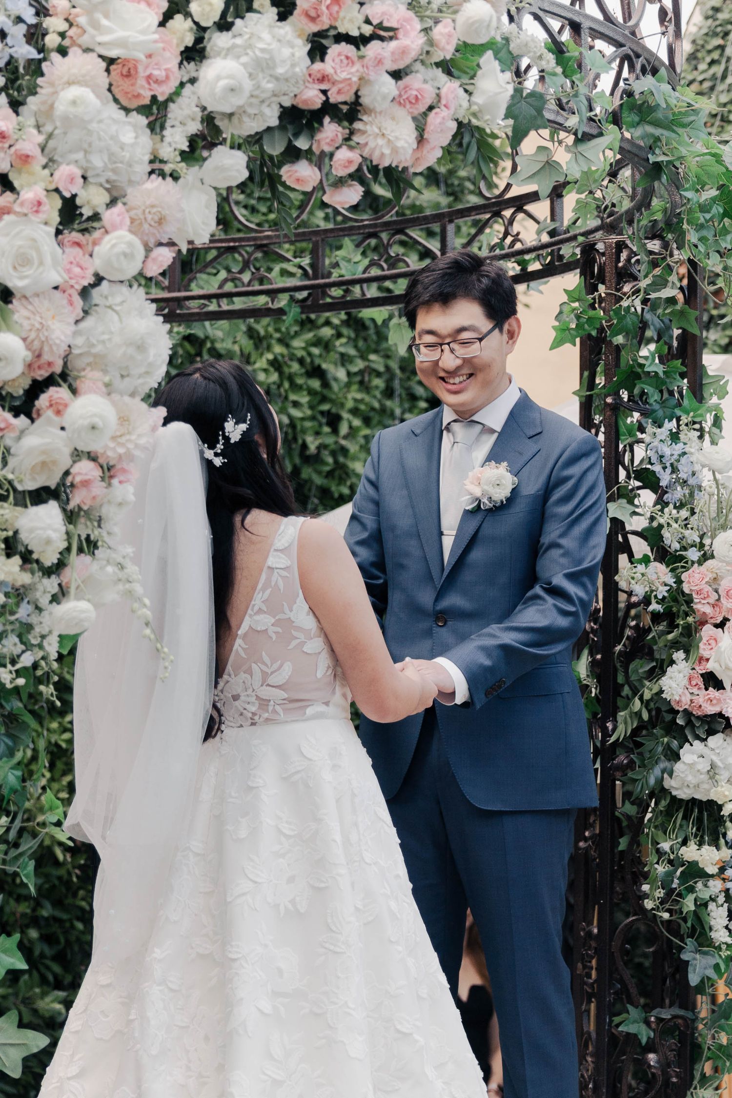 A wedding ceremony under a beautiful floral arch with pink and white roses and greenery.