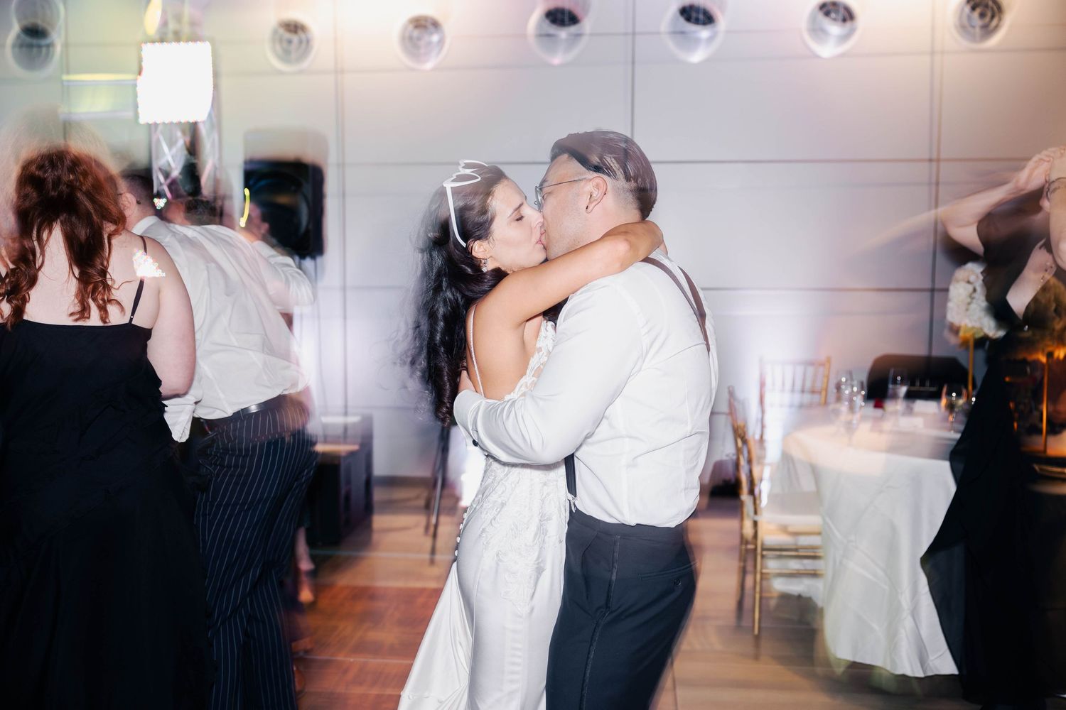 Couples dancing together in formal attire at an elegant ballroom event with white decor and lighting.