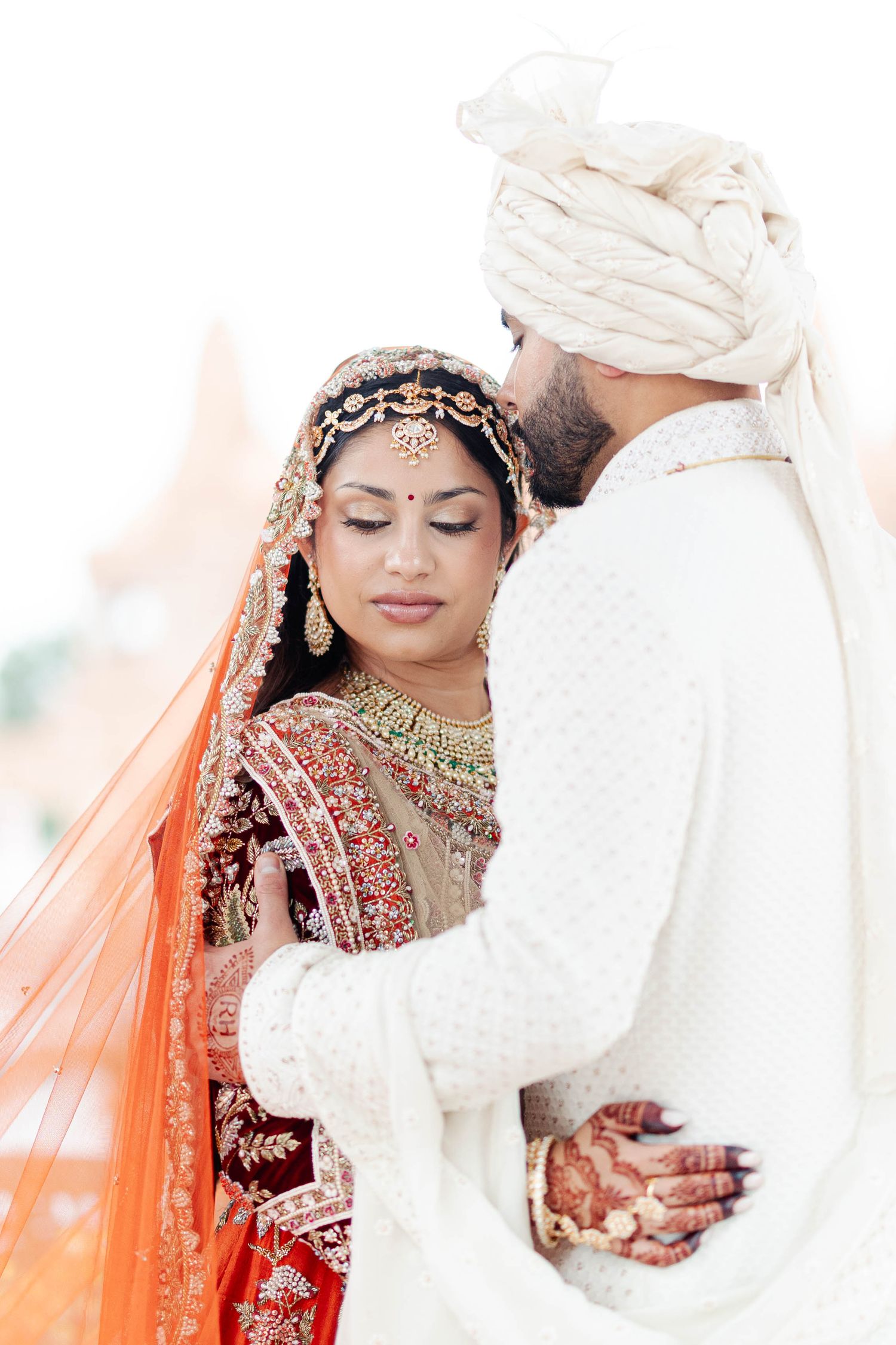 Traditional Indian wedding ceremony with bride in red lehenga and groom in white sherwani performing rituals.