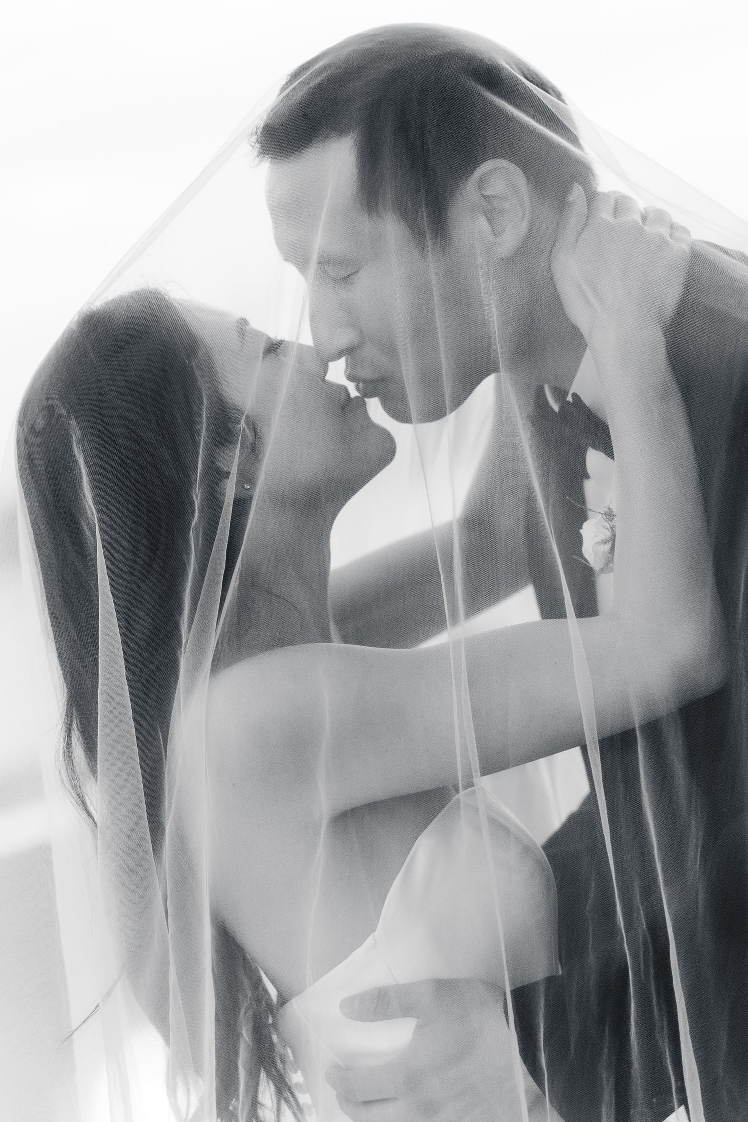 Black and white photo of bride and groom sharing romantic moment under wedding veil.