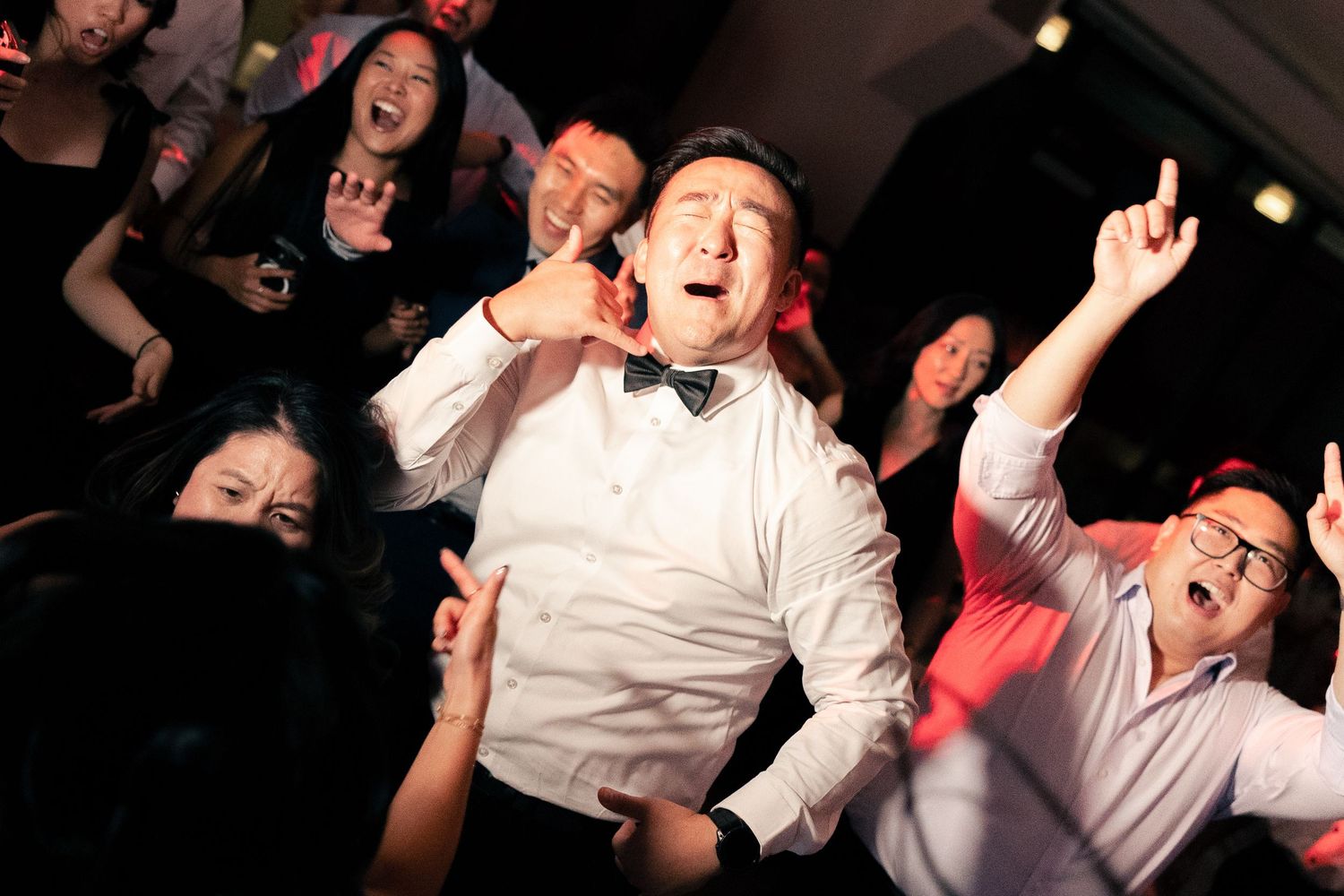Joyful man in bow tie dancing at a lively wedding reception party with guests celebrating around him.