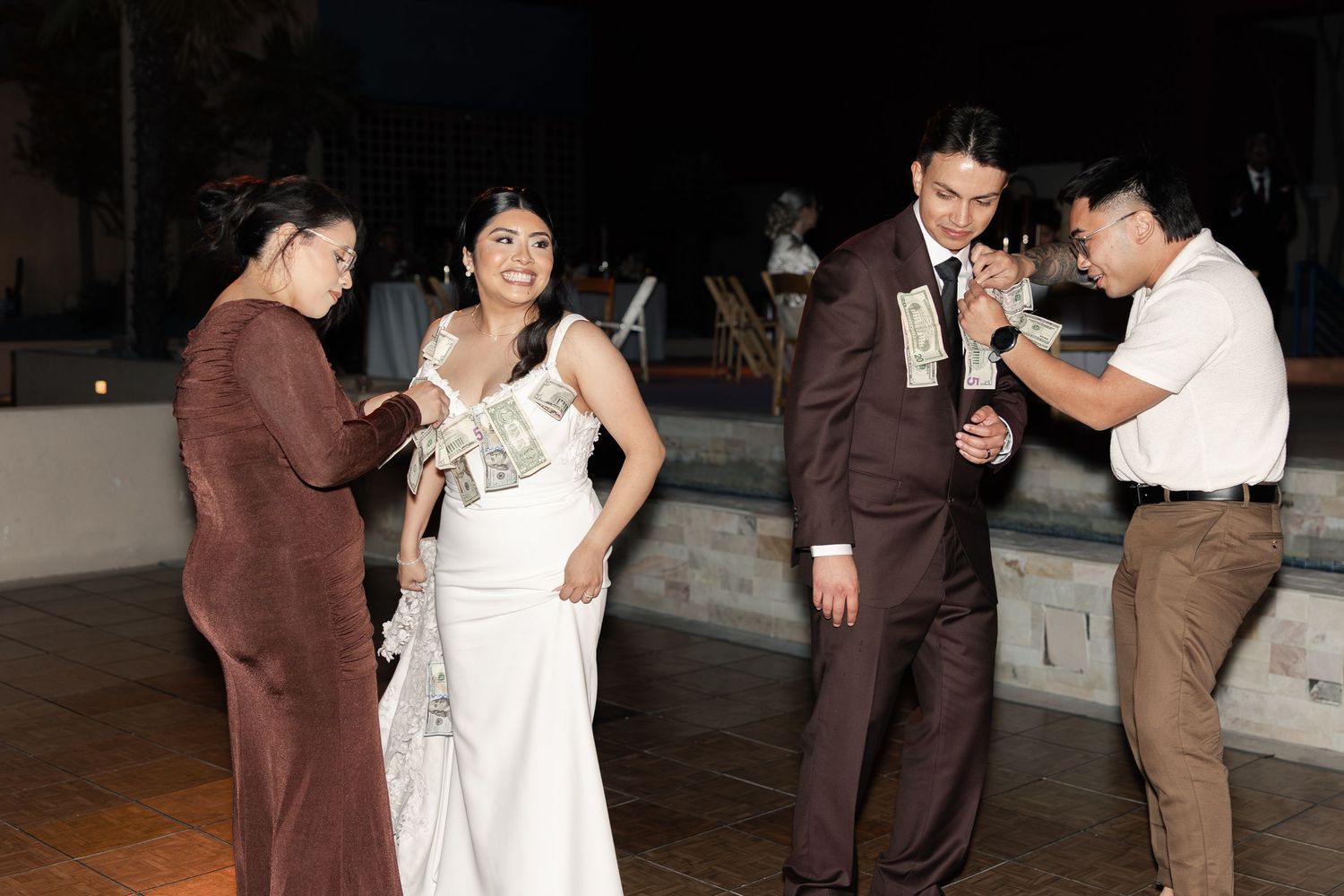 Bride and groom having money pinned to their wedding attire during a traditional money dance at their reception.