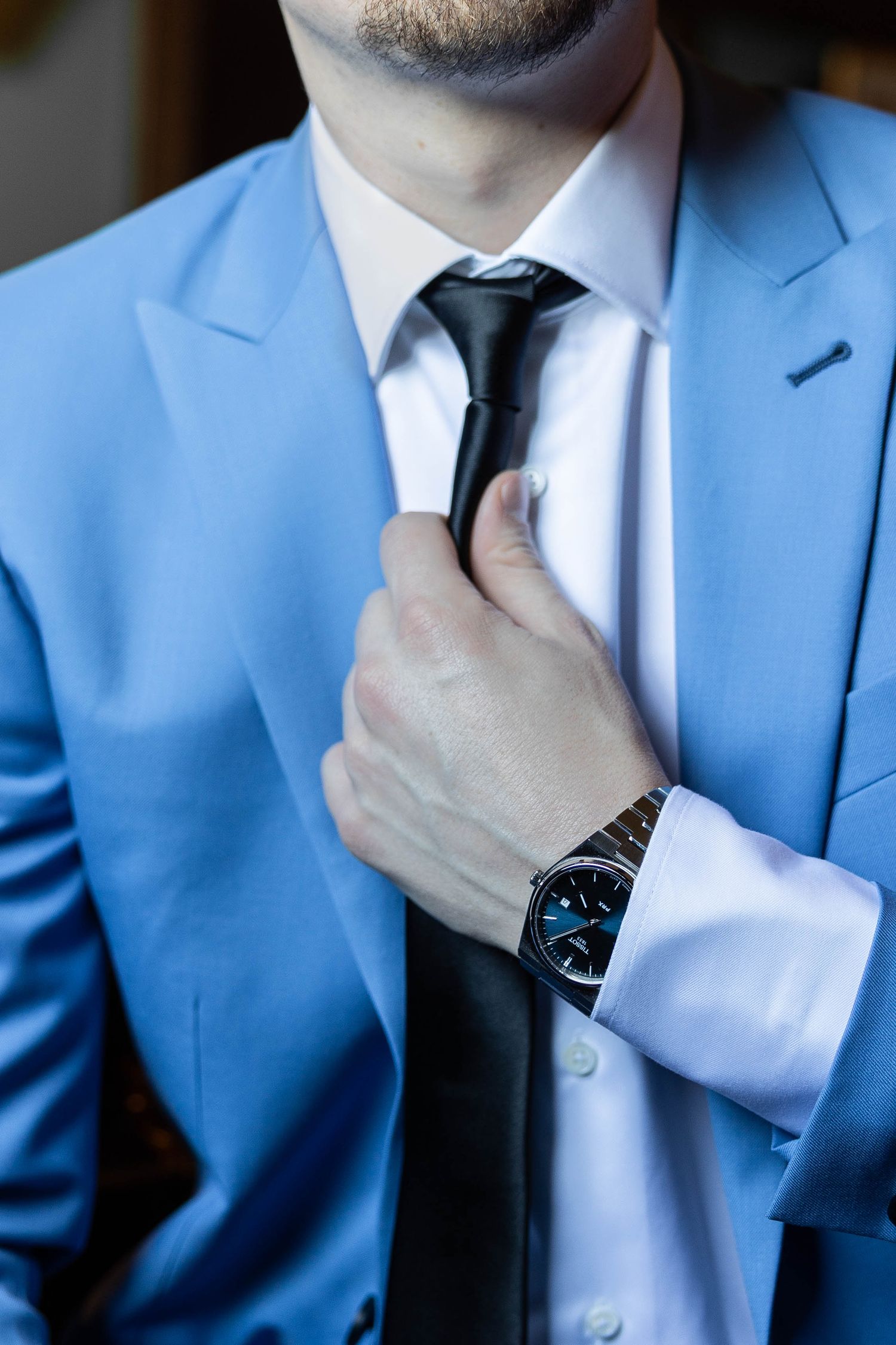 Close-up of a light blue suit jacket with black tie and wristwatch detail.