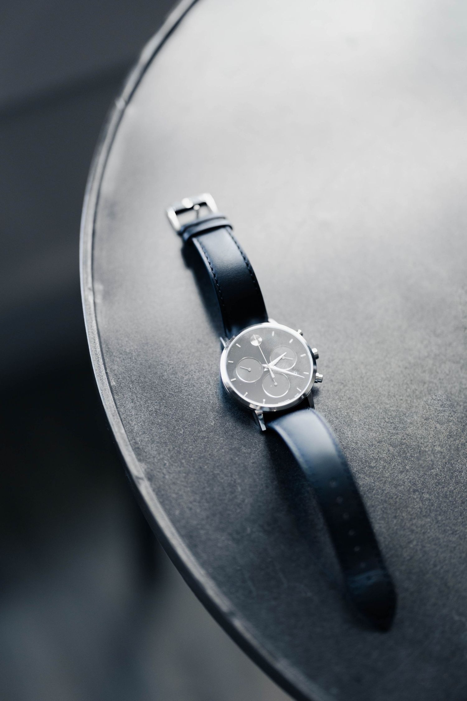 Classic wristwatch with black leather band shown in dramatic lighting against dark surface.