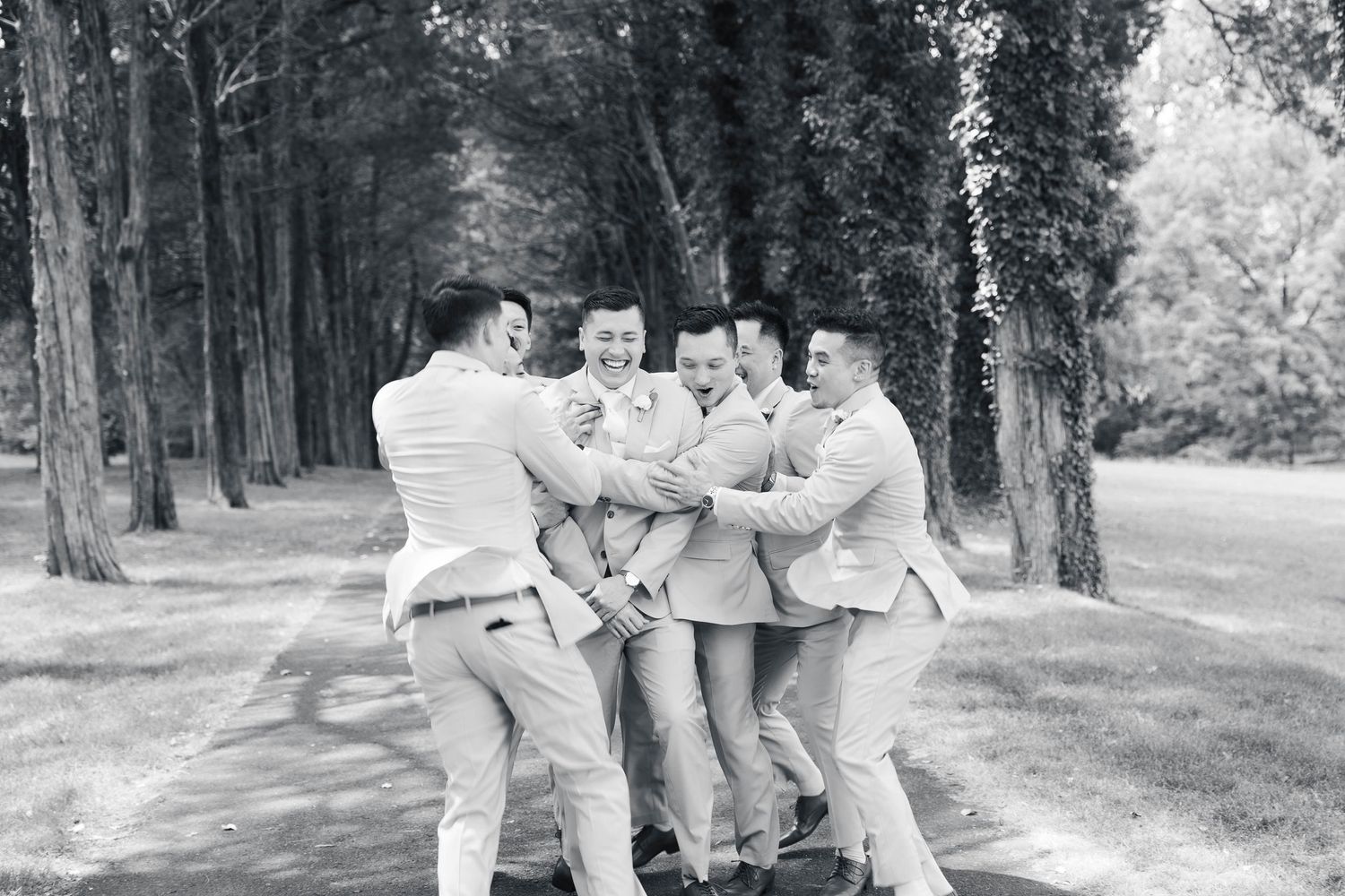 Groomsmen share candid moments on a wooded path during wedding photography.