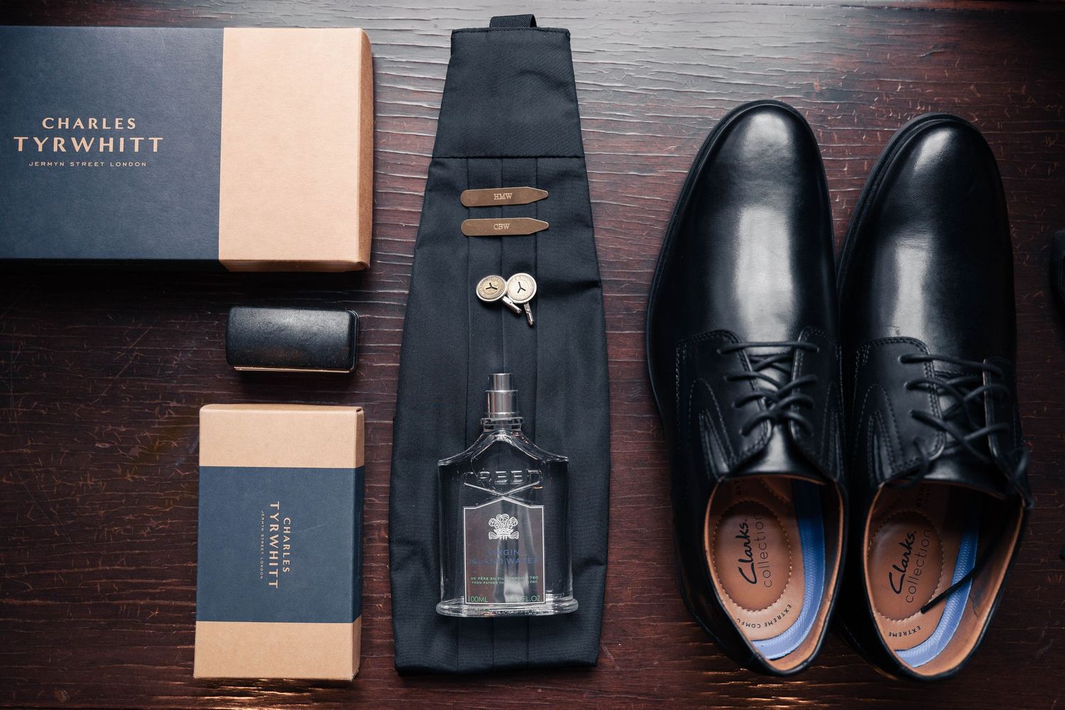 Black leather dress shoes with decorative perforations arranged in a row against a dark wooden background.
