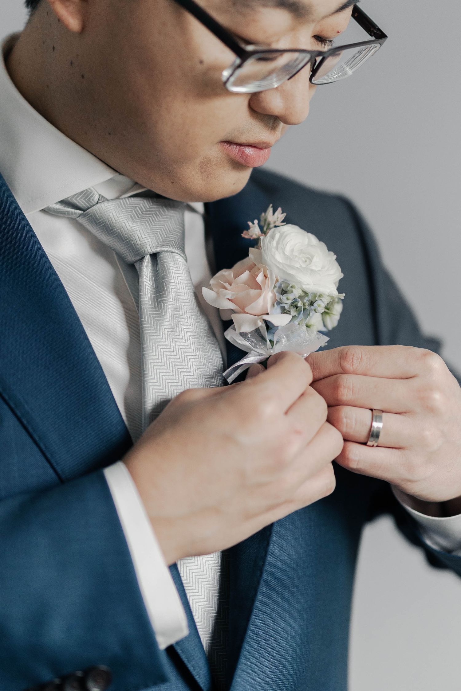 Close-up sequence of groom adjusting boutonniere on navy suit with light gray tie.