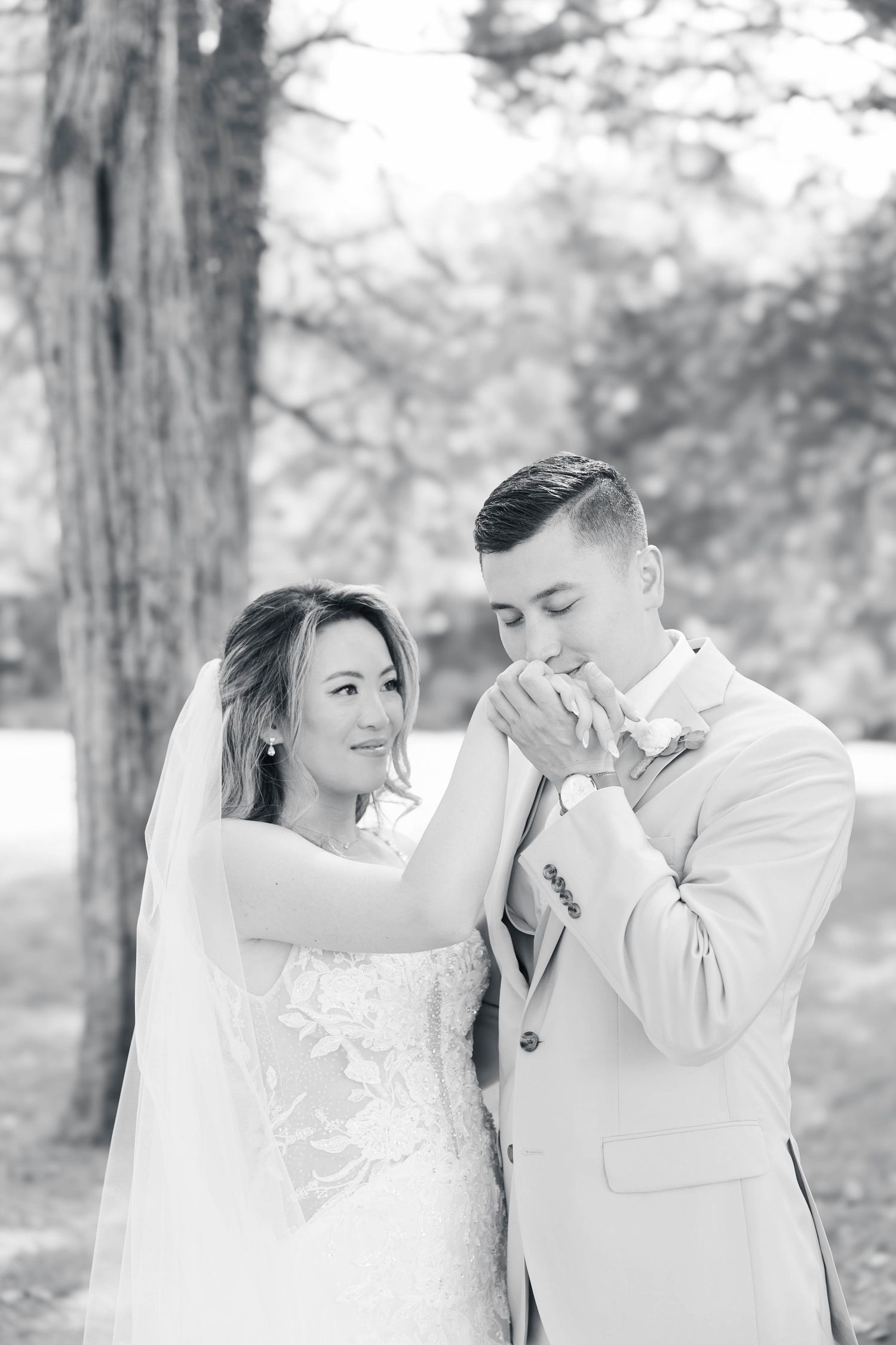 A romantic wedding moment captured as the groom kisses the bride's hand in a forest setting.