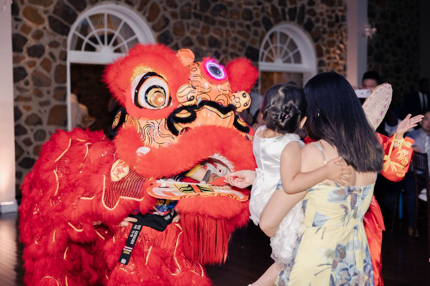 Lion dancers in red costumes interacting with wedding guests during performance.
