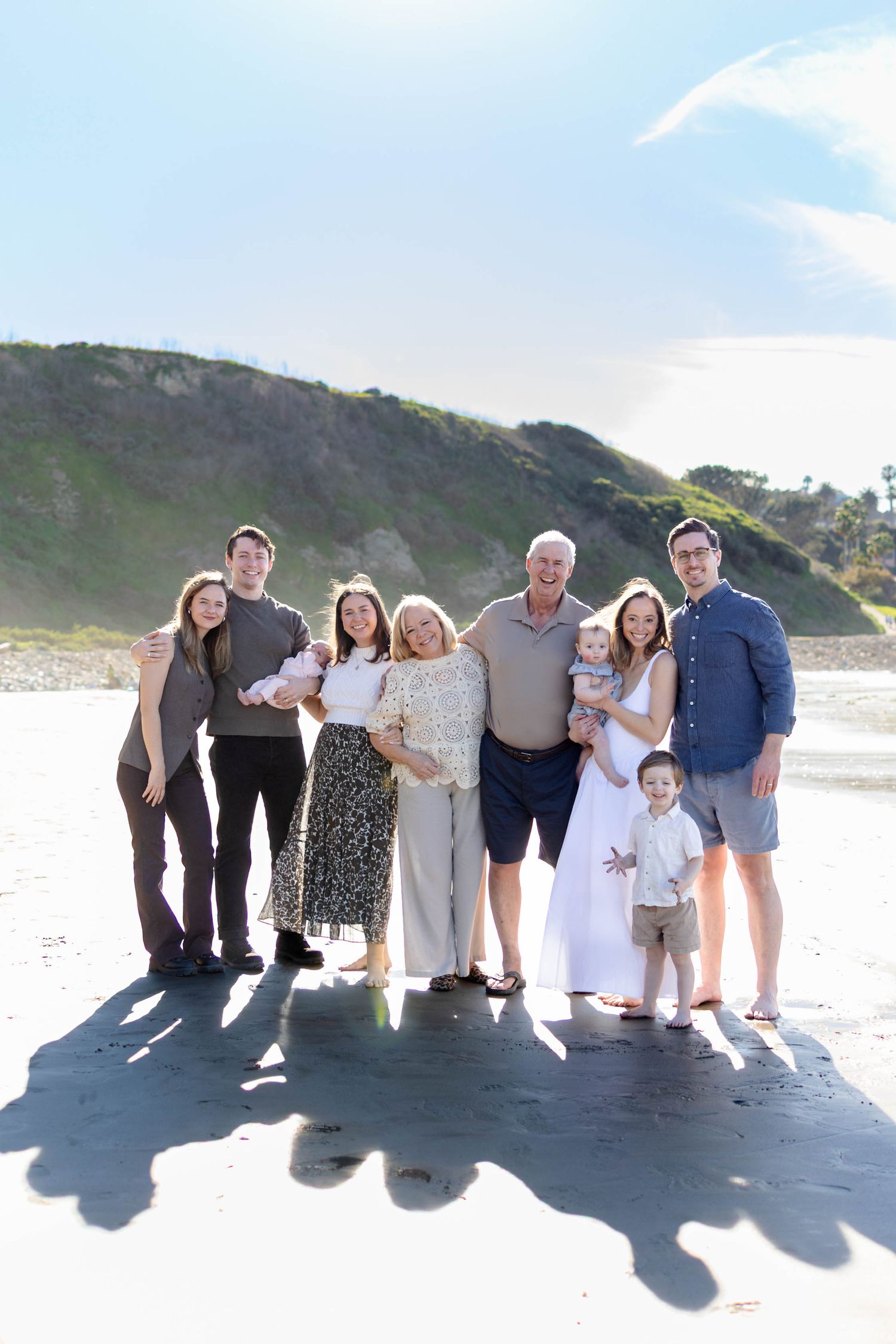 A group of people stand together on a beach casting long shadows against the sand during golden hour.