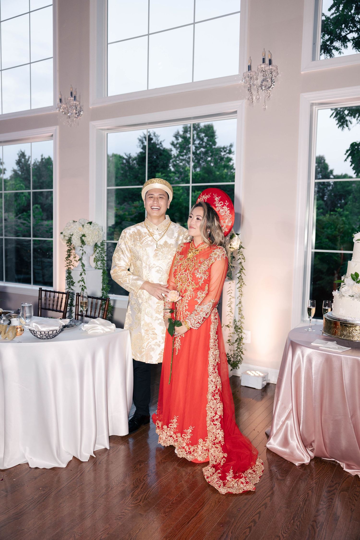 Wedding reception venue decorated with white linens and large windows overlooking green trees.