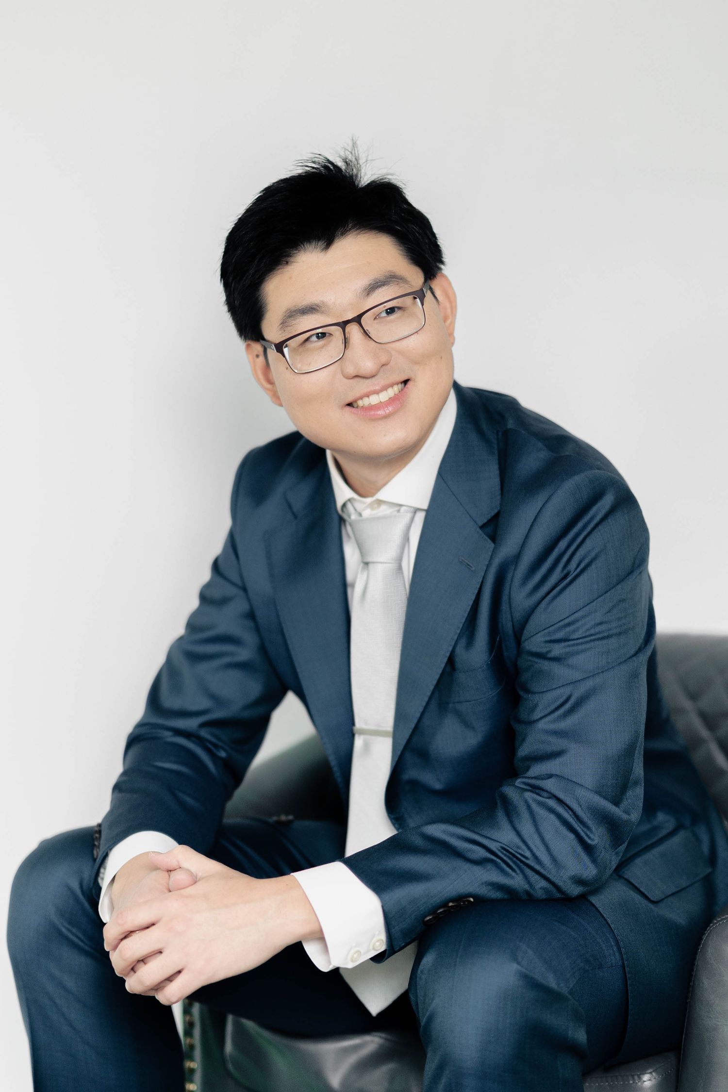 Casual business portraits showing relaxed poses on dark furniture against white backdrop.