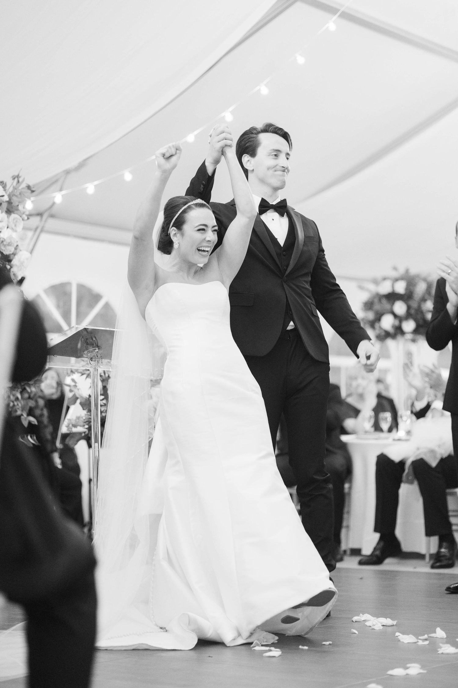 Joyful newlyweds share their first dance under a white tent at an outdoor wedding reception.