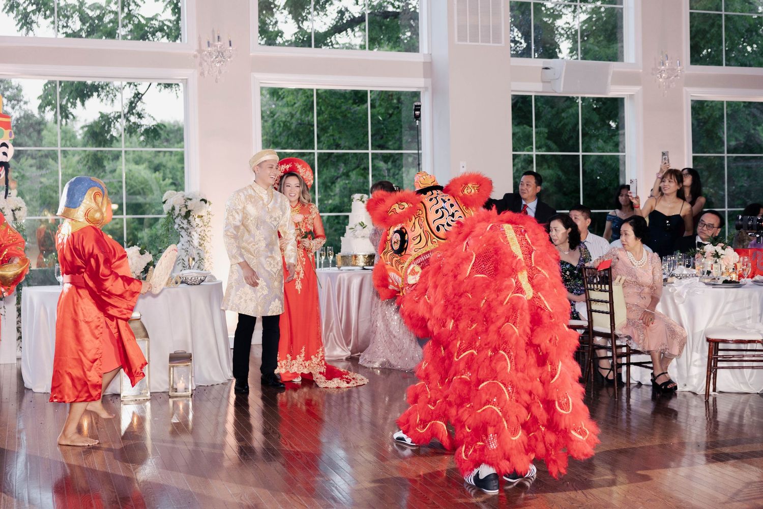 Chinese lion dancers perform in a bright wedding reception hall with stone walls and large windows.