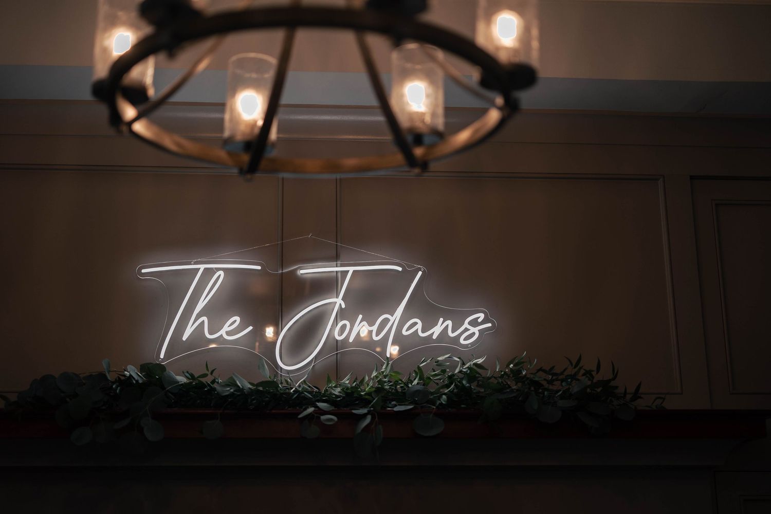 Rustic chandelier with glowing lights and neon sign in a dark reception space.