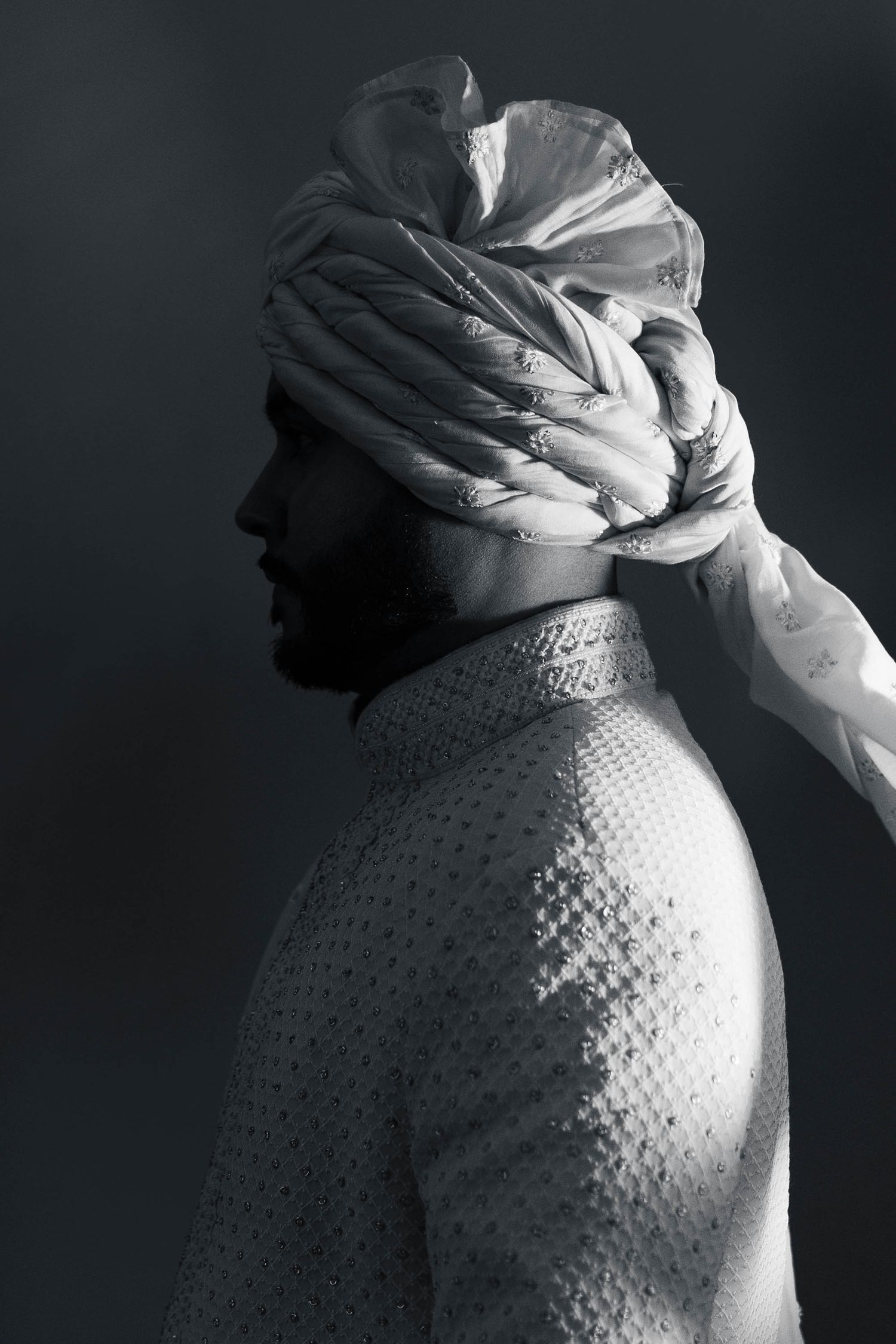 Black and white artistic portrait showing a side profile silhouette wearing an ornate textured garment and wrapped headdress.