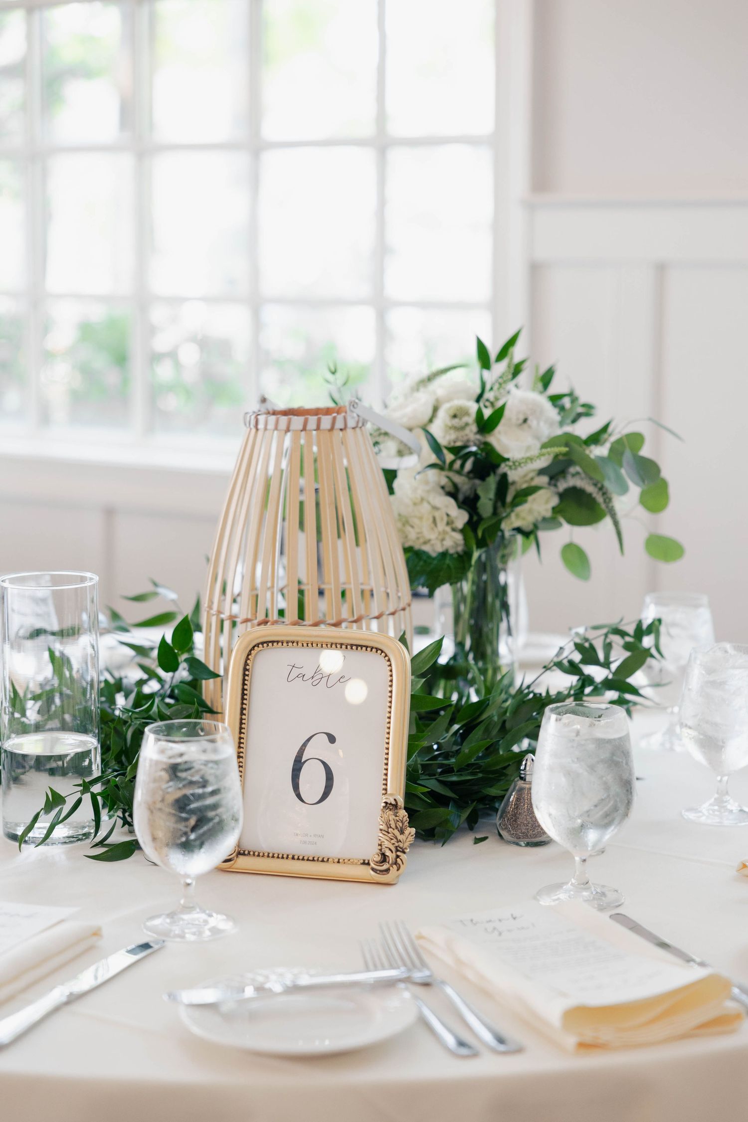 Elegant white wedding table setting with greenery centerpieces and wooden accent lanterns for decoration.
