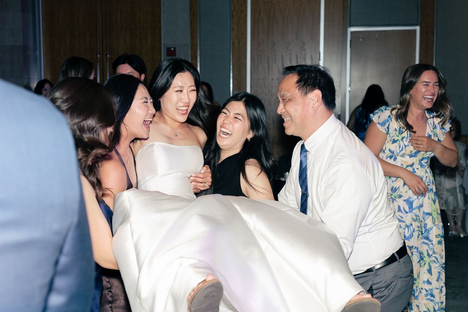 Friends joyfully lift a bride in a white gown during a lively wedding reception celebration.