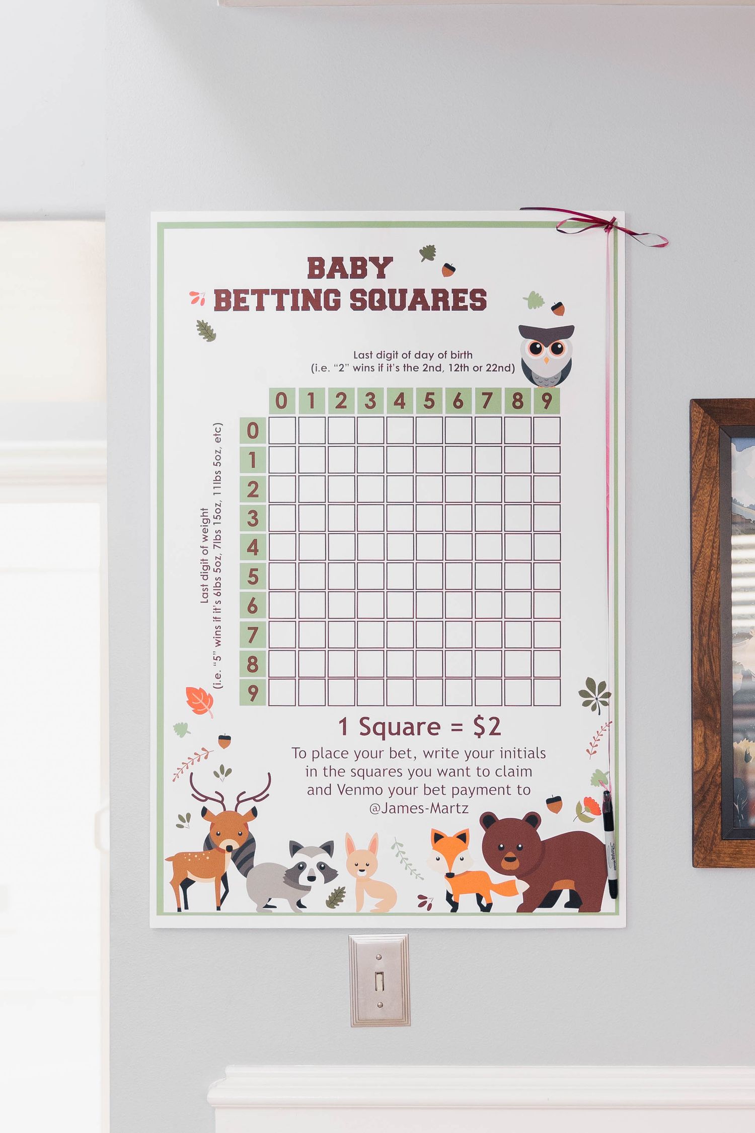 Baby shower betting squares game board with woodland animal theme and grid layout for party predictions displayed on wall.