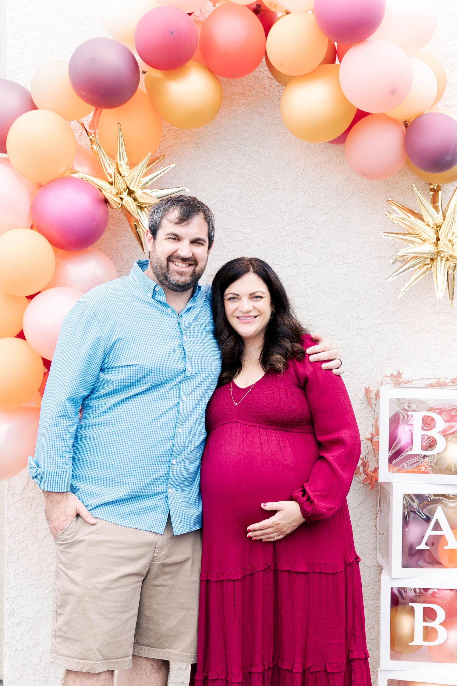 Festive baby shower scene with peach and purple balloon arch and decorative BABY blocks against white wall.