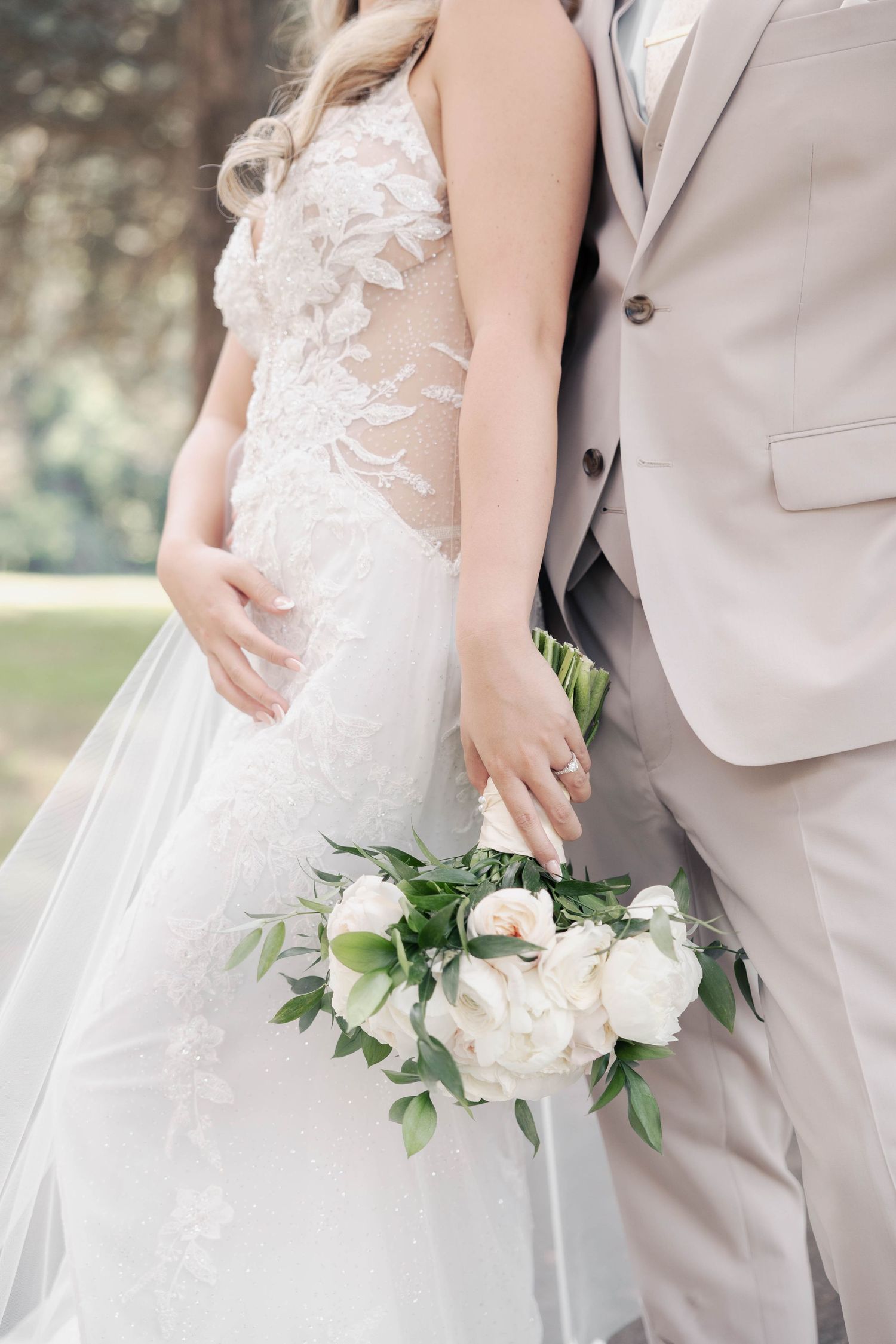 Intimate wedding details showing lace dress and bouquet against light beige suit.