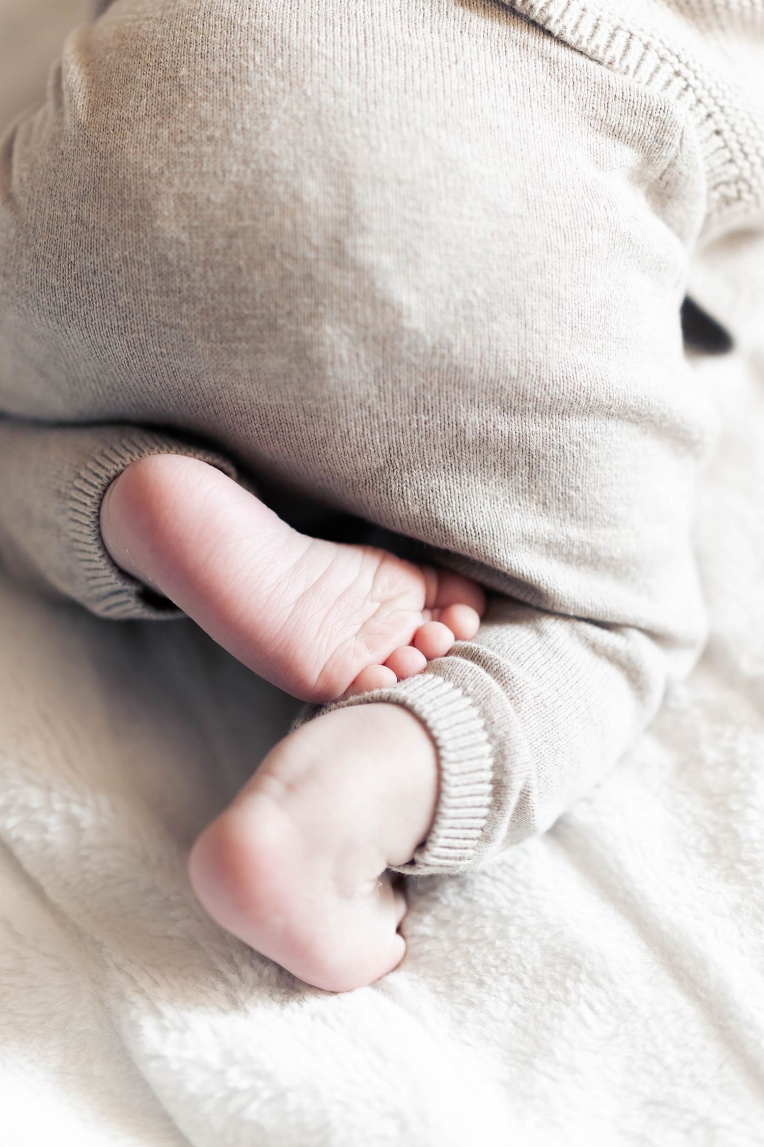Tiny baby feet peek out from under a soft knitted blanket.
