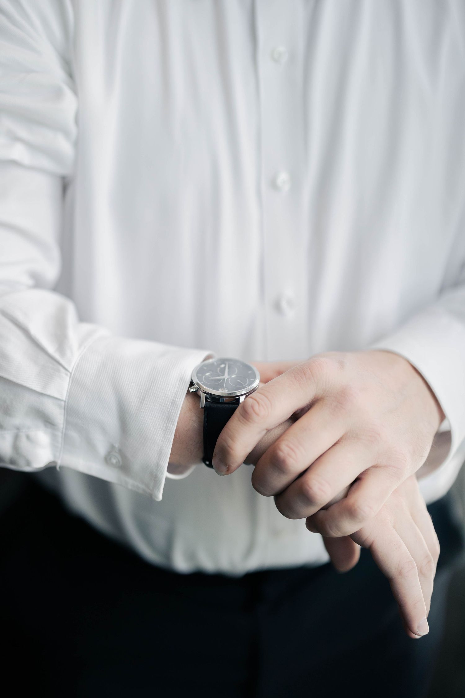 Person in white dress shirt checking wristwatch.